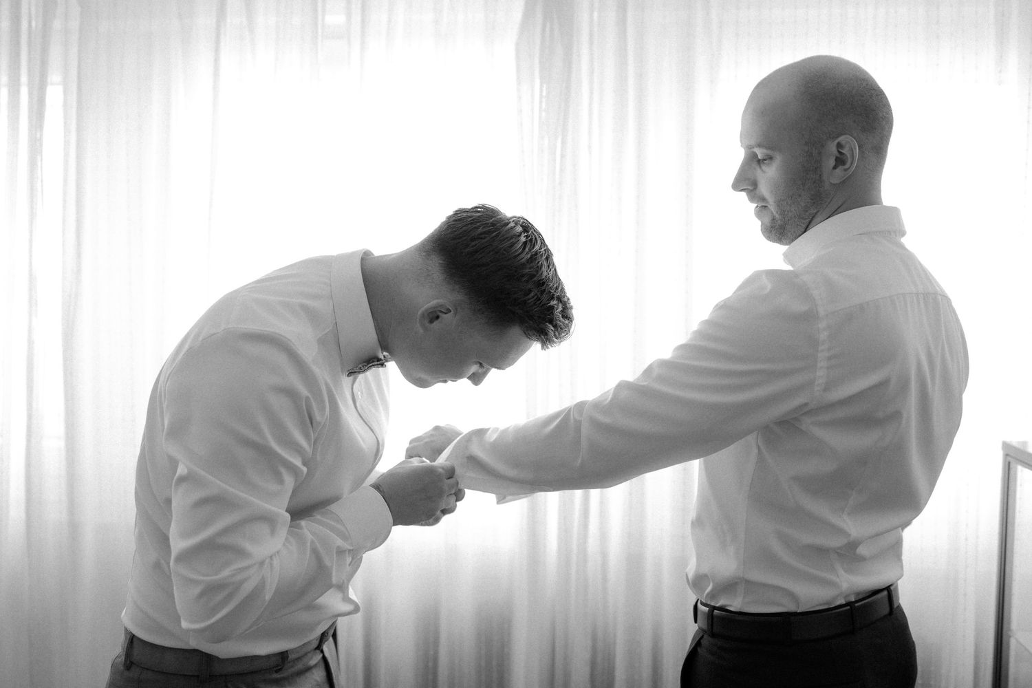 Intimate black and white moment of wedding preparation between two people.