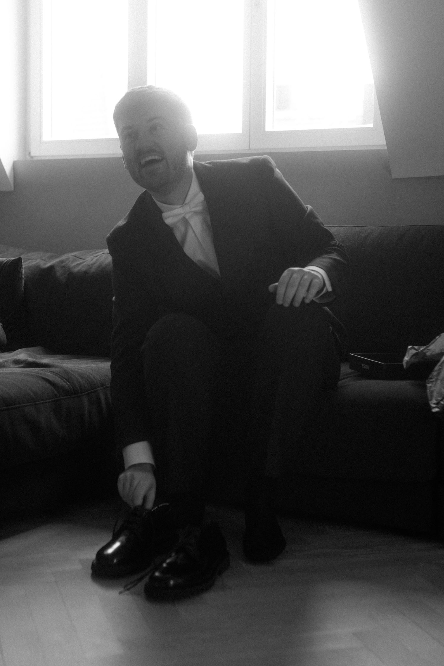 Person in formal attire sitting on a dark couch near a bright window.