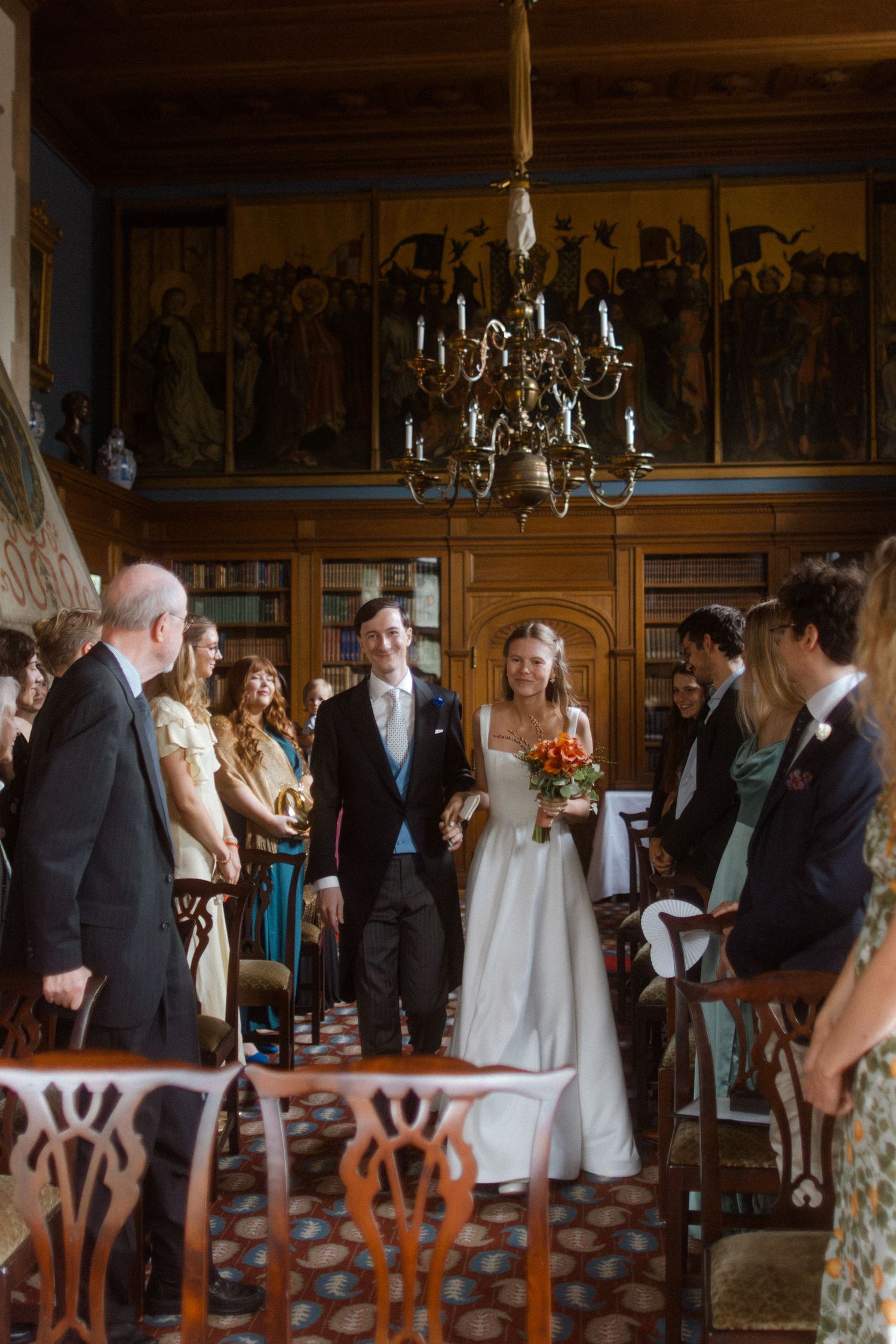 Wedding celebration taking place in a vintage library setting with wooden chairs.