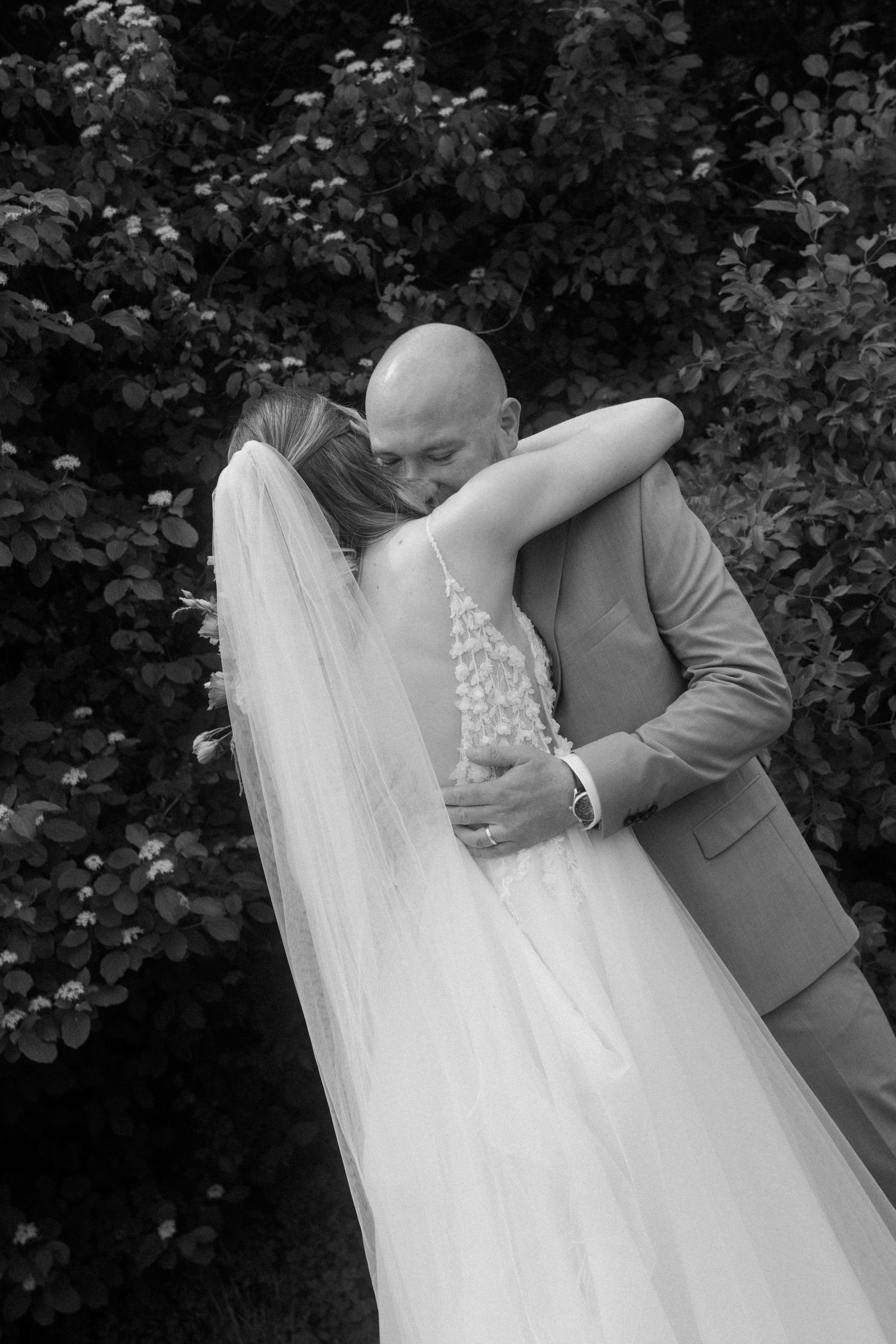 A black and white wedding photo series captures intimate moments between a couple against foliage.