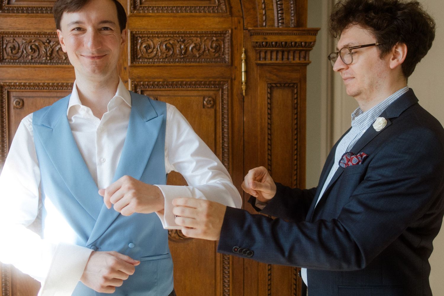 Two people in formal attire adjusting clothing in an elegant room with wood paneling.