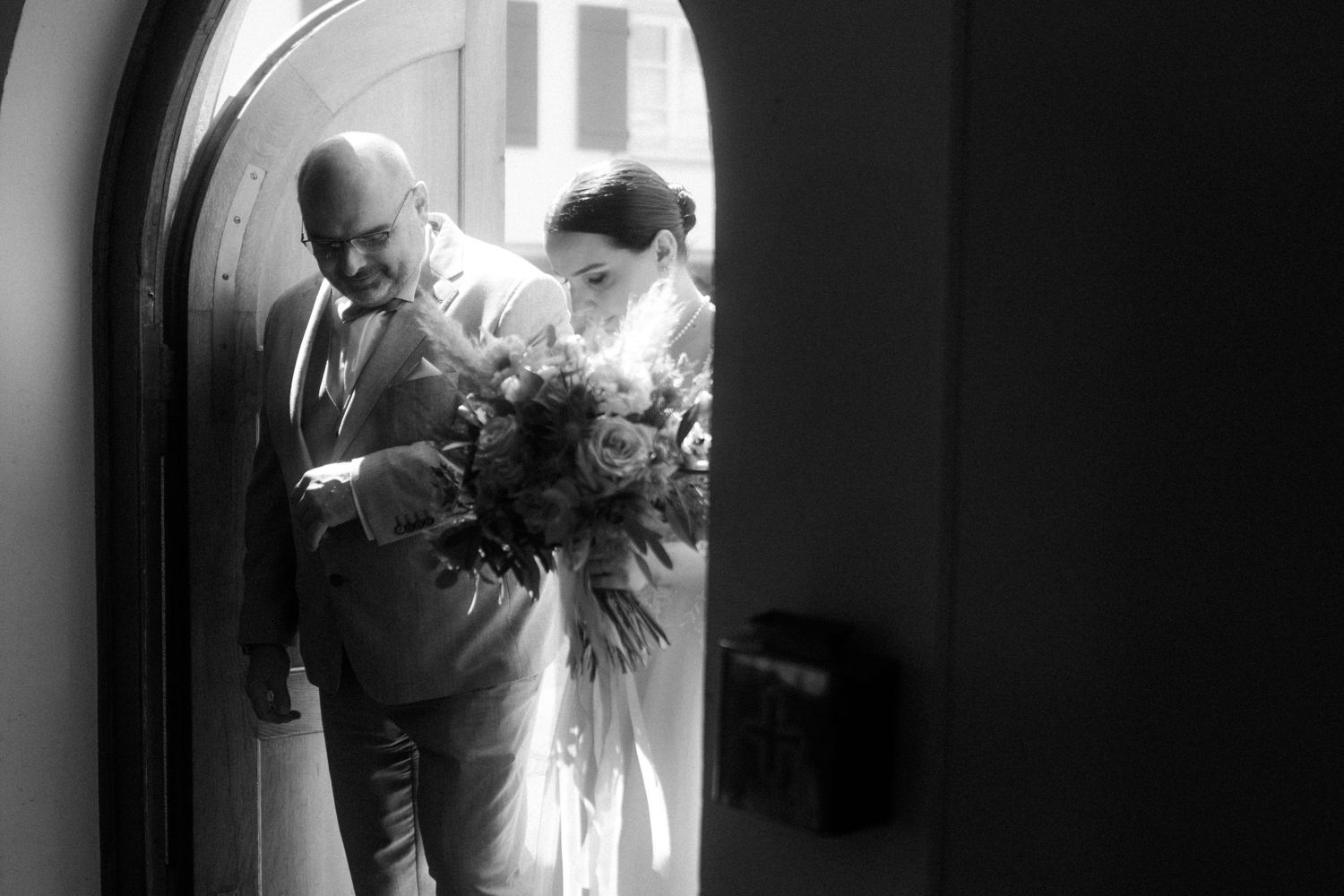 Black and white photograph of wedding processional through arched doorway.