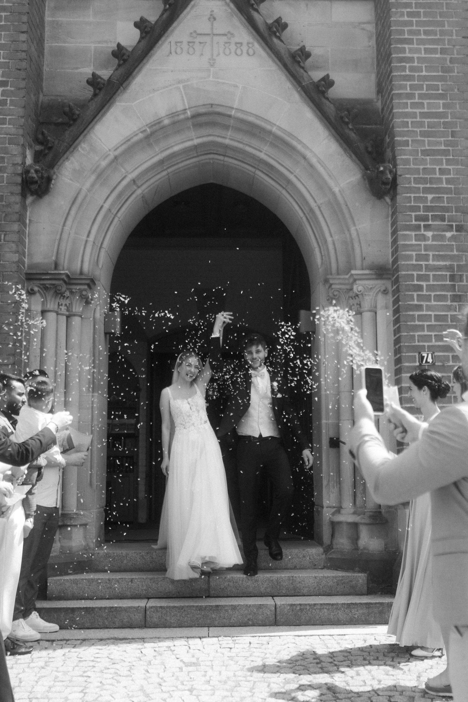 Black and white capture of bride and groom showered with confetti on church steps.