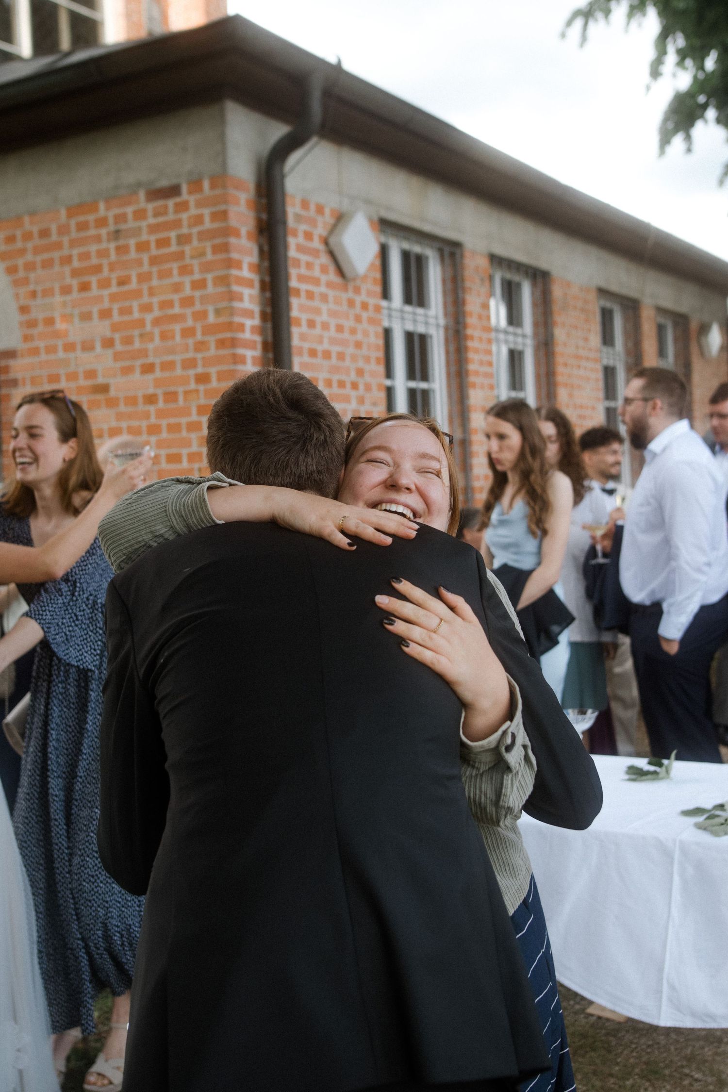Close-up of warm embrace at outdoor wedding celebration near exposed brick wall.