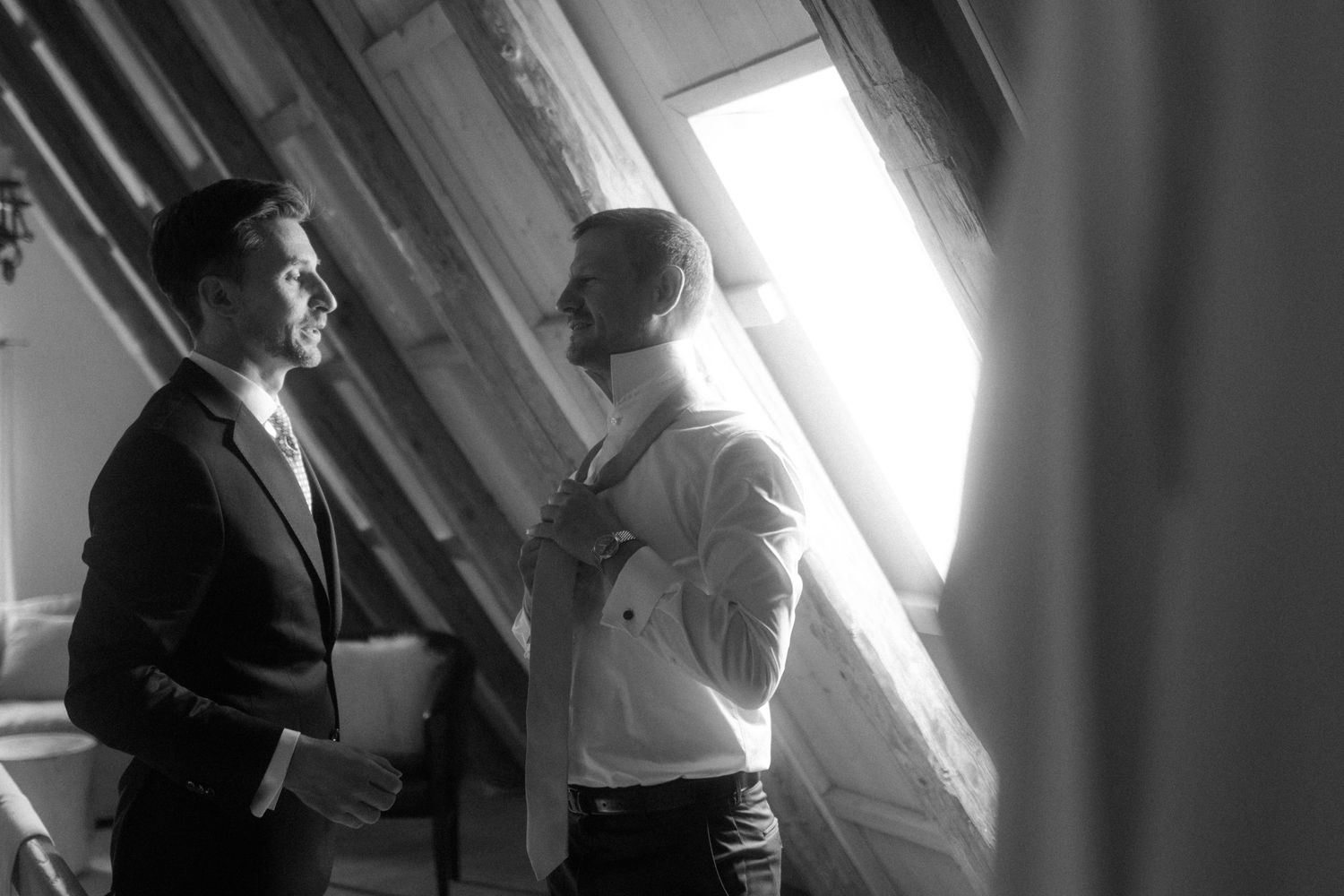 Two figures standing in sunlit attic room with exposed beams.