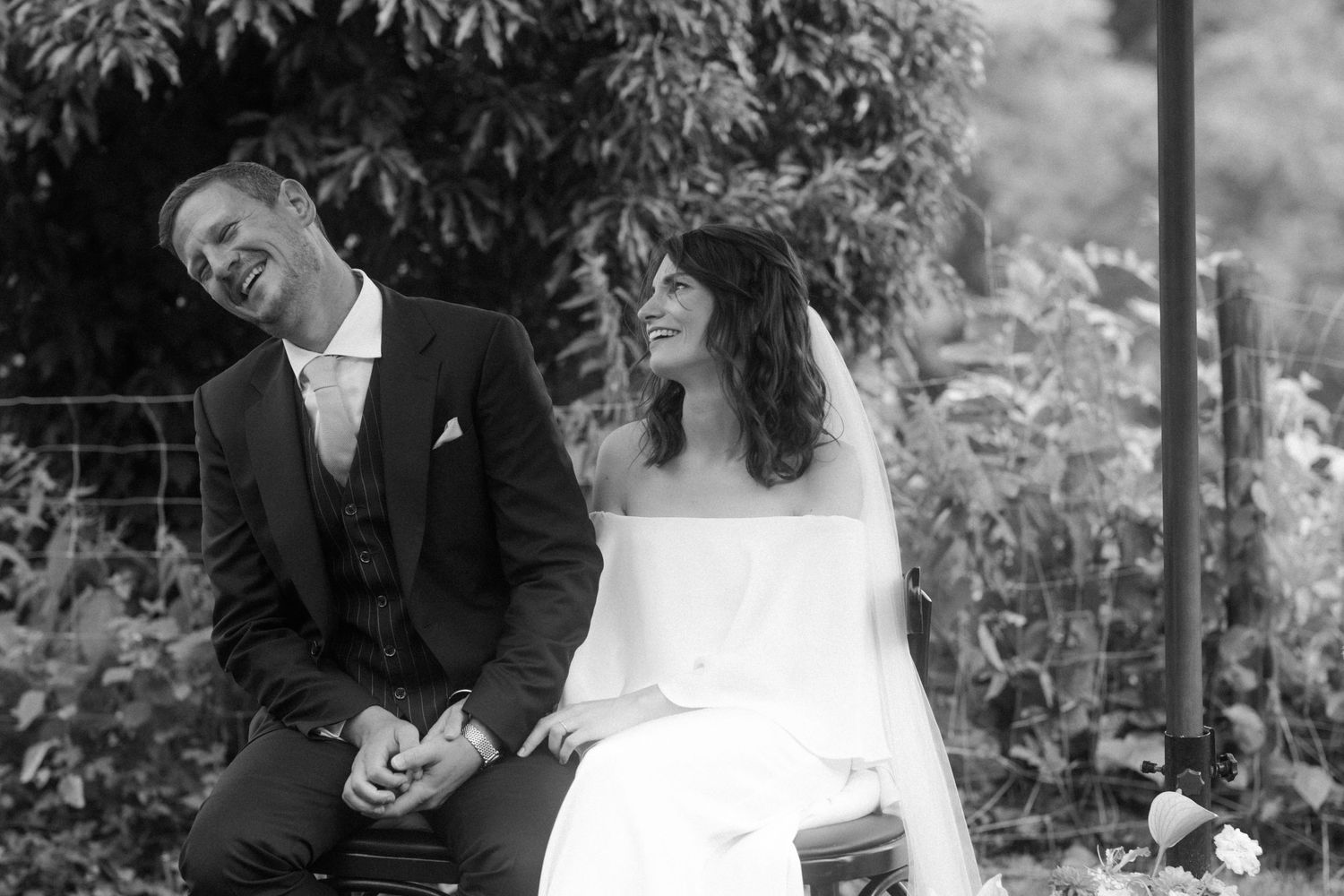 A black and white wedding photo capturing a candid moment between newlyweds in a garden setting.