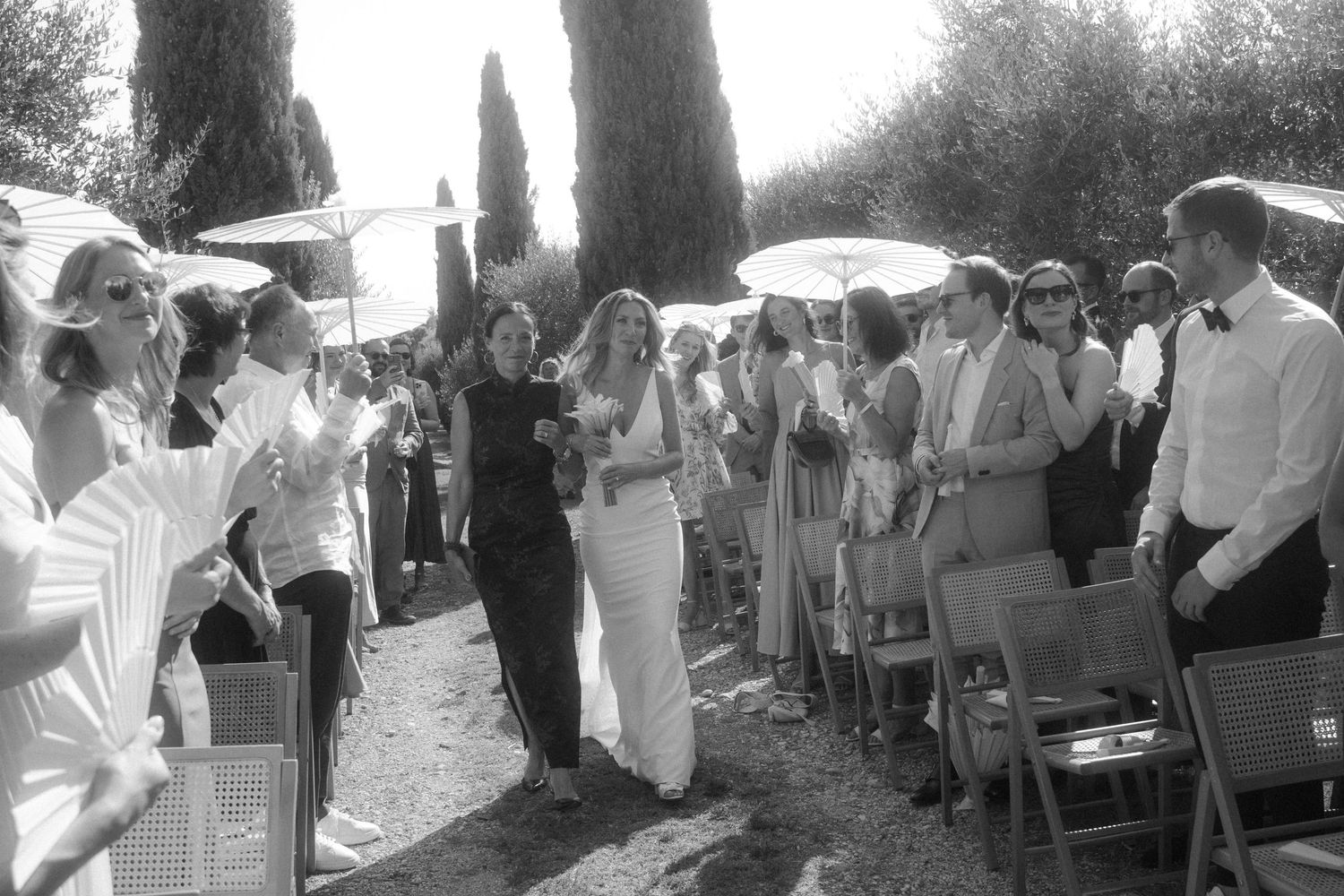 Wedding guests gathered along a rustic path lined with tall cypress trees in Italy.