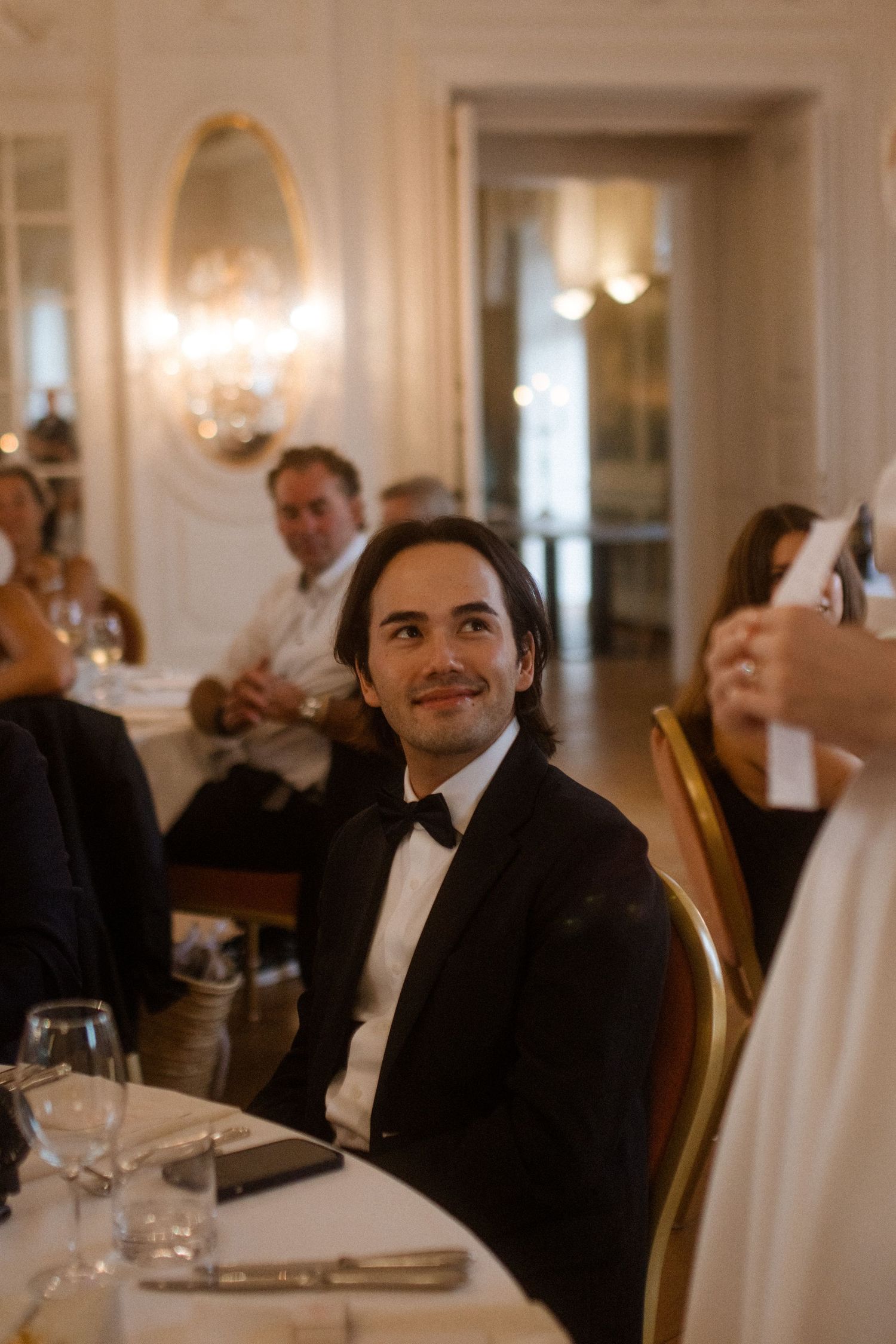 Wedding guests seated at dining tables in a luxurious white ballroom.