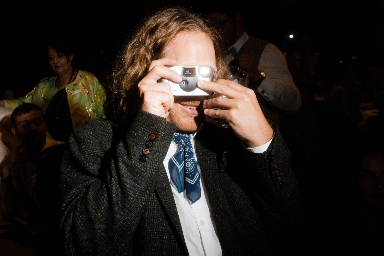 Child in suit and tie photographing with a disposable camera at a formal event.