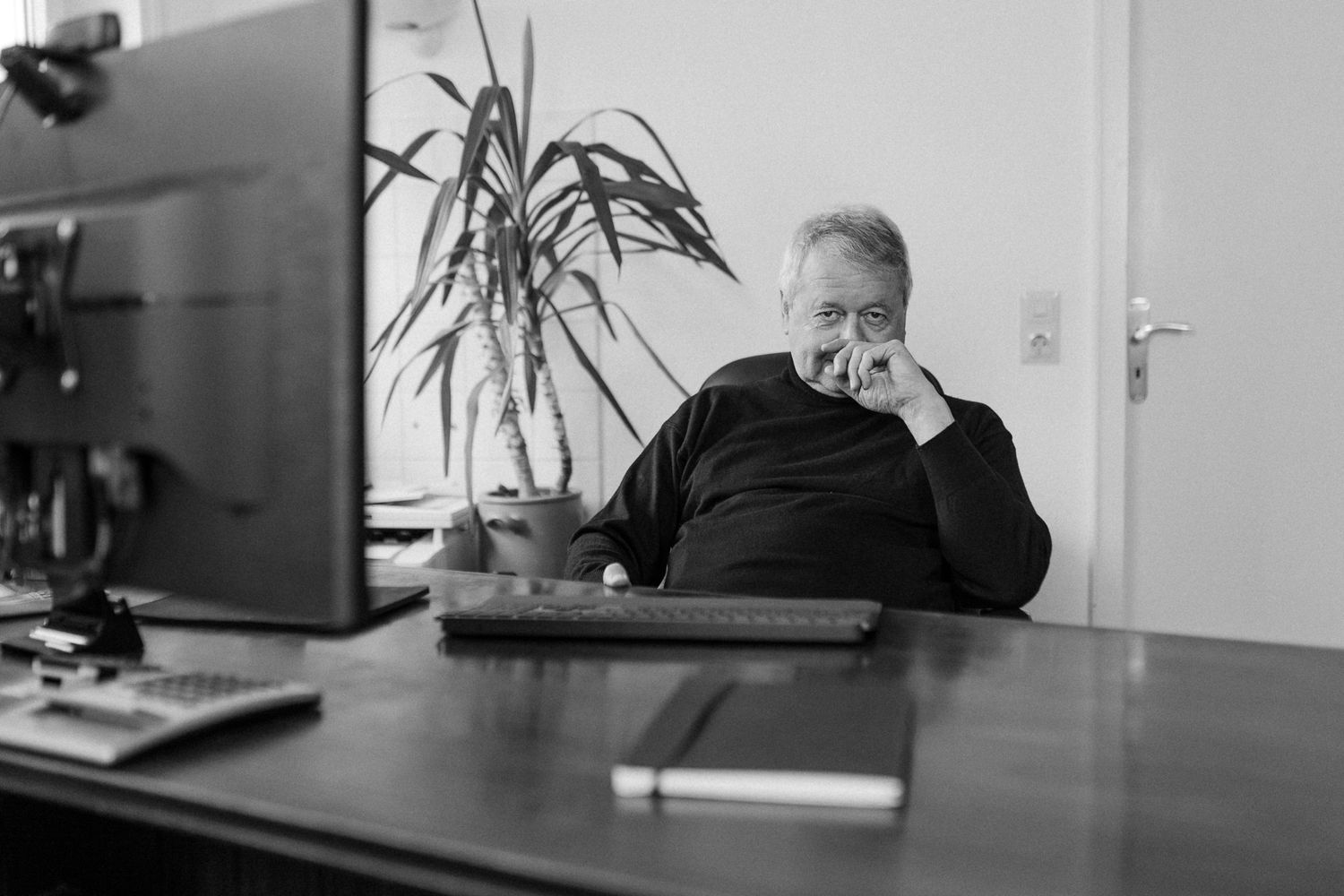 Modern office interior with desk, plant, and window lighting captured in black and white.