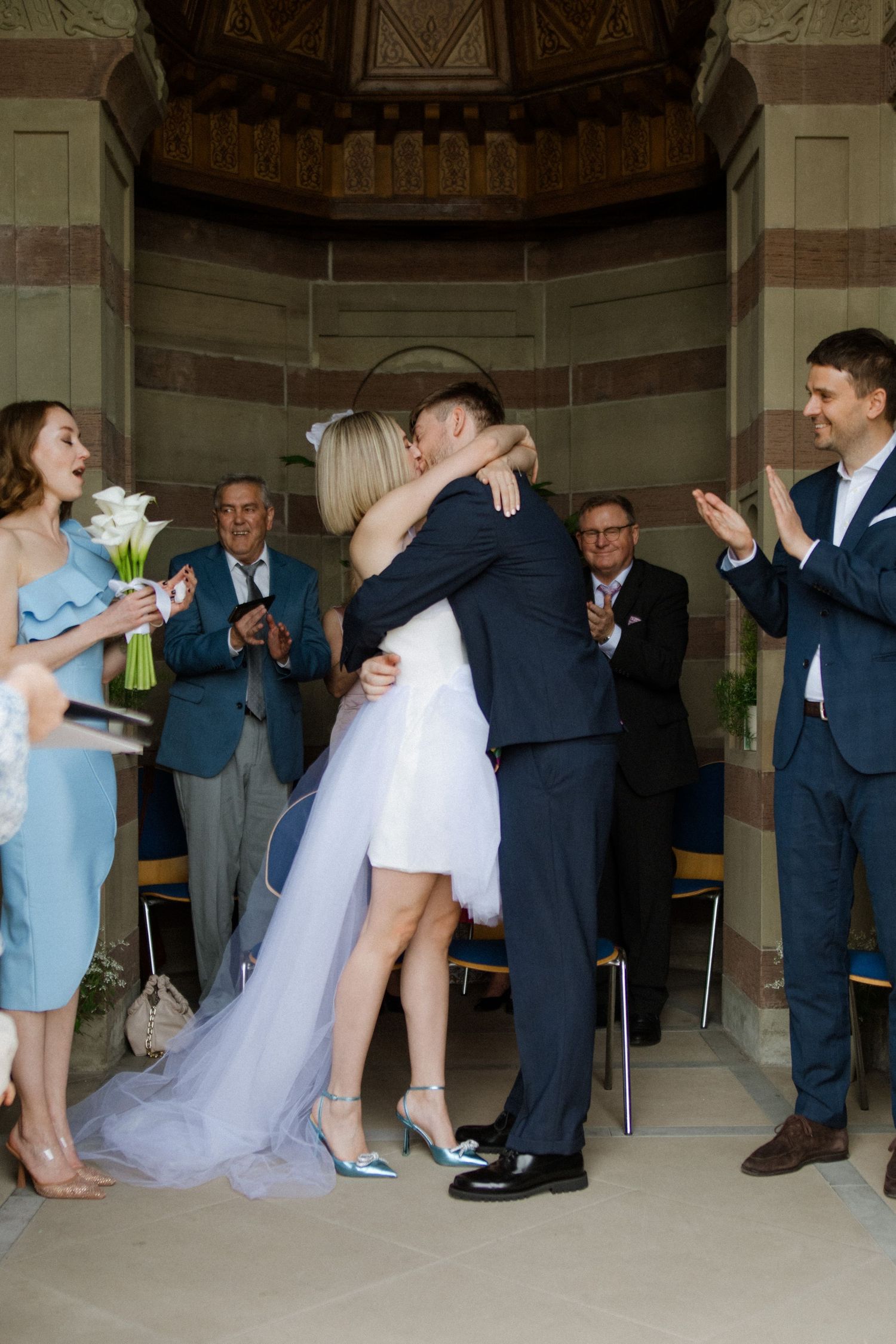 Wedding party dancing and celebrating in a grand indoor venue with blue bridesmaid dresses.
