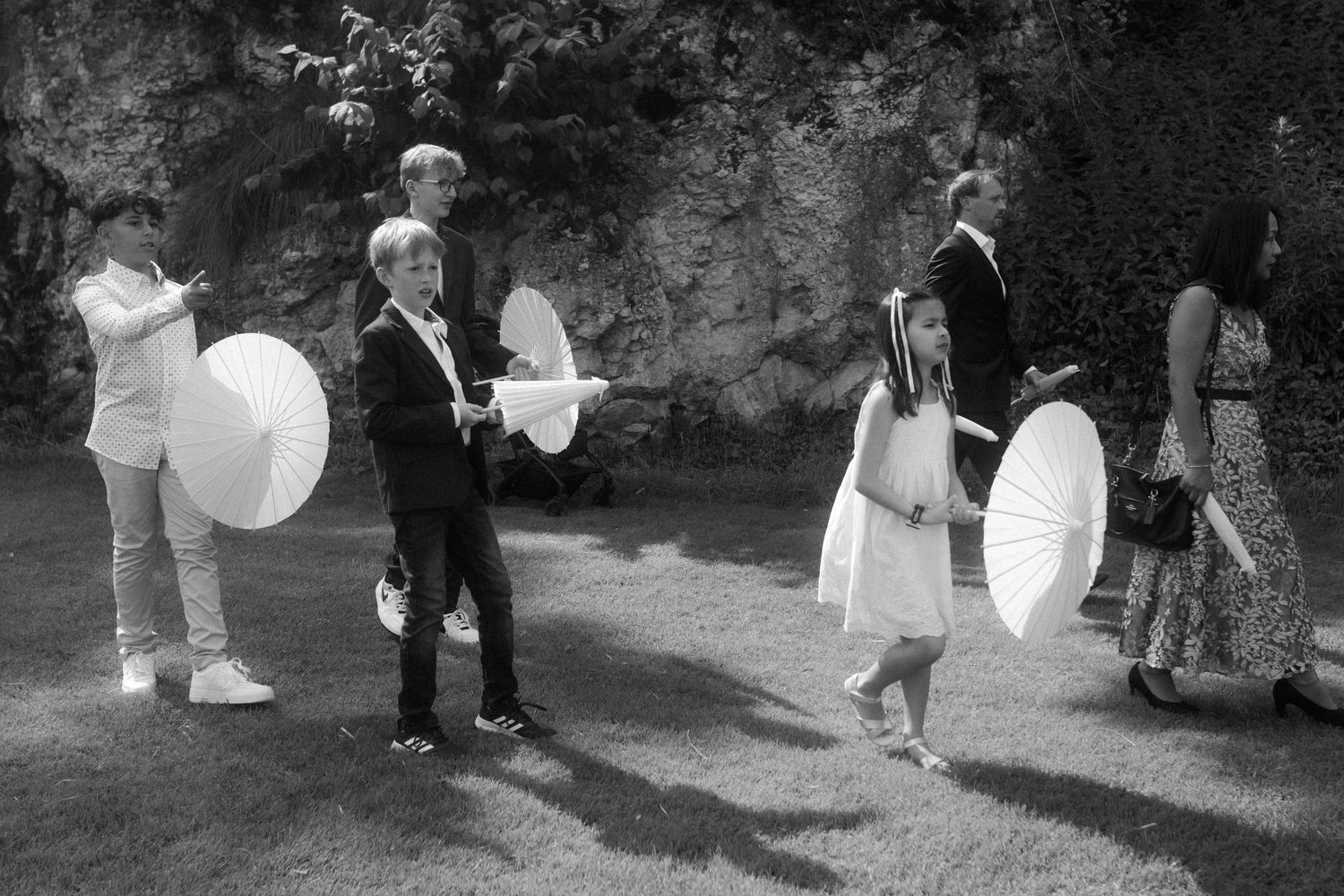 Wedding guests holding white parasols gather in a garden setting.