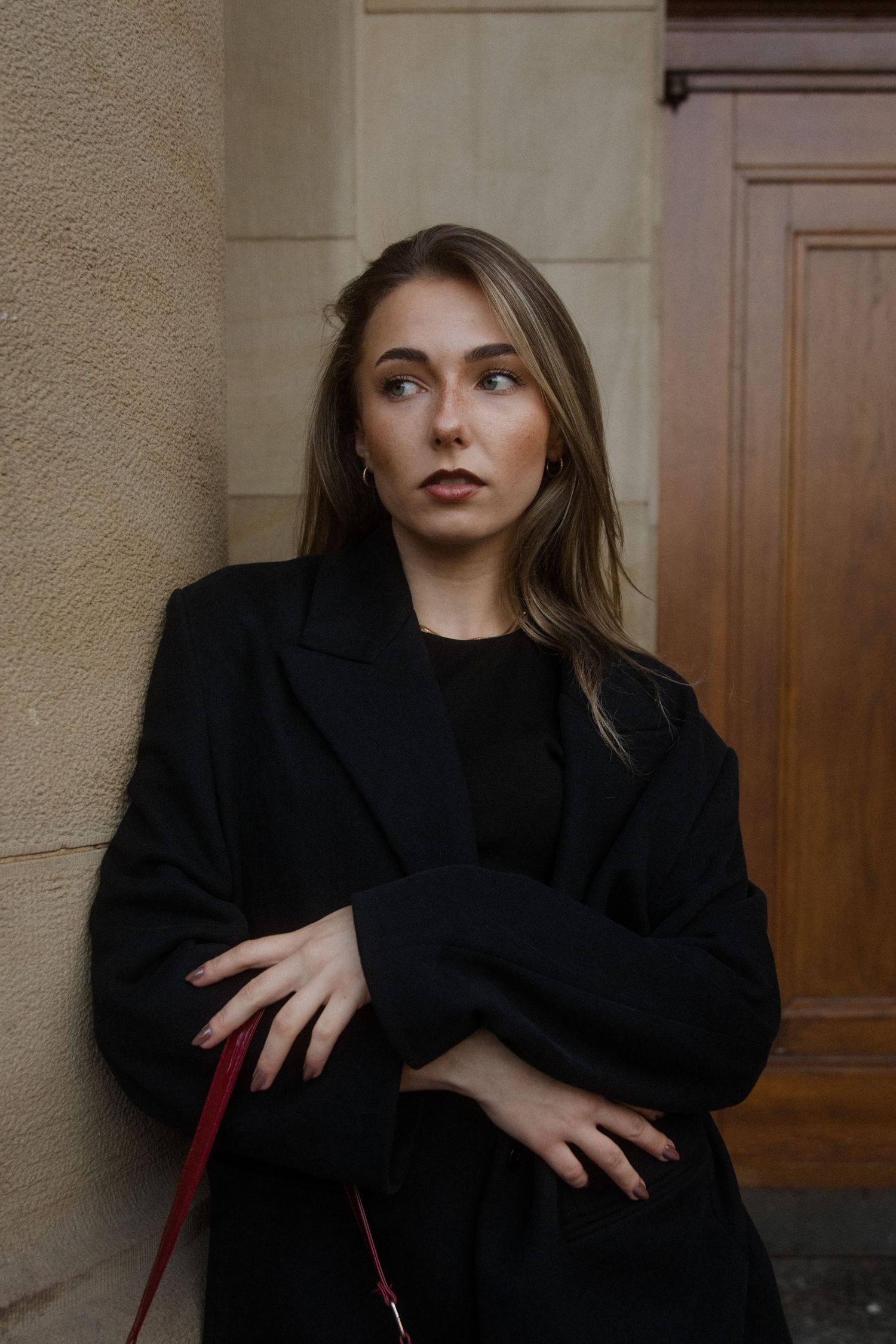 A series of moody fashion portraits showing a person in a black blazer against a beige wall with wooden door details.
