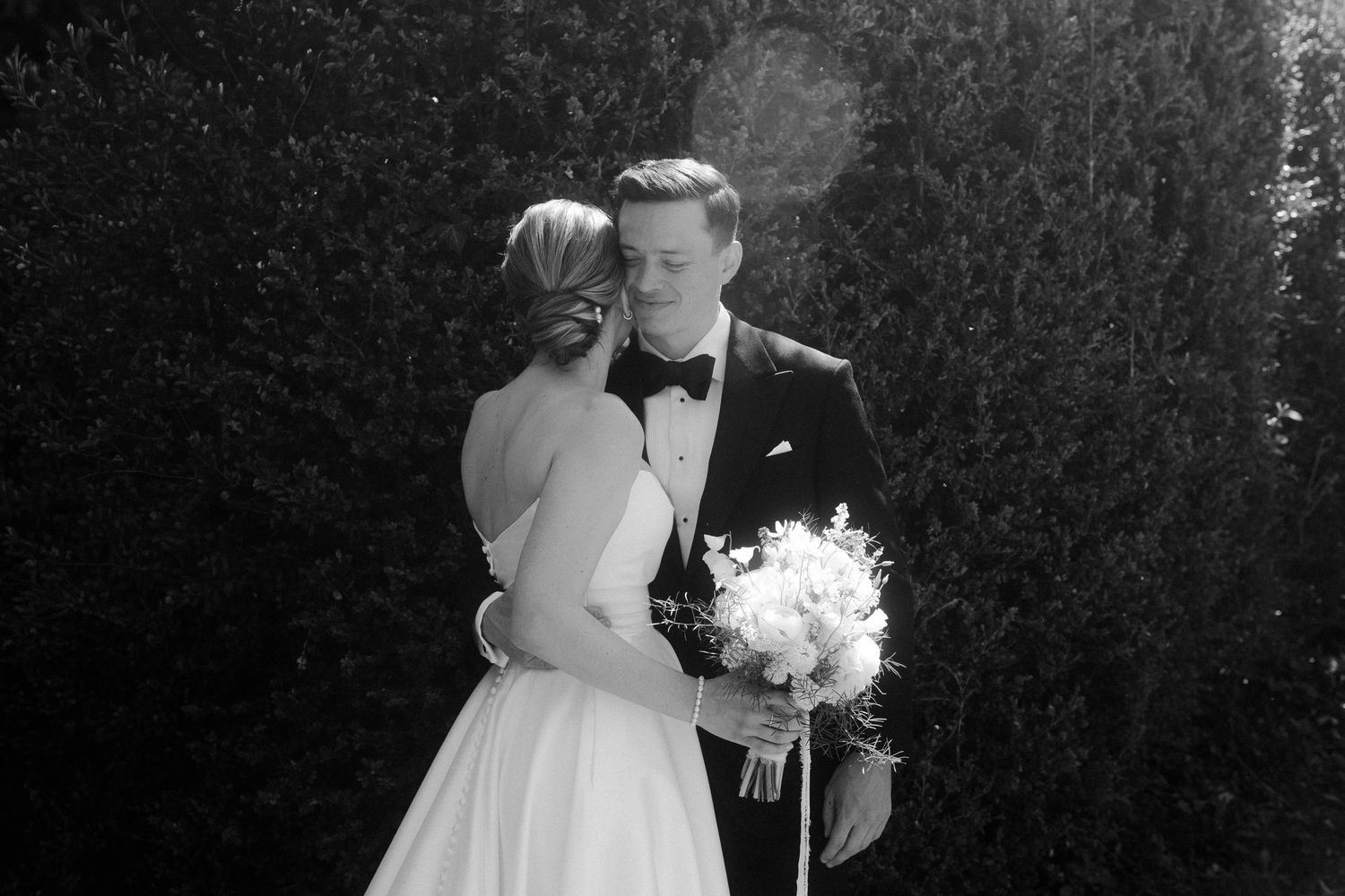 Black and white wedding photo of bride and groom sharing a kiss outdoors, bride holding white bouquet.