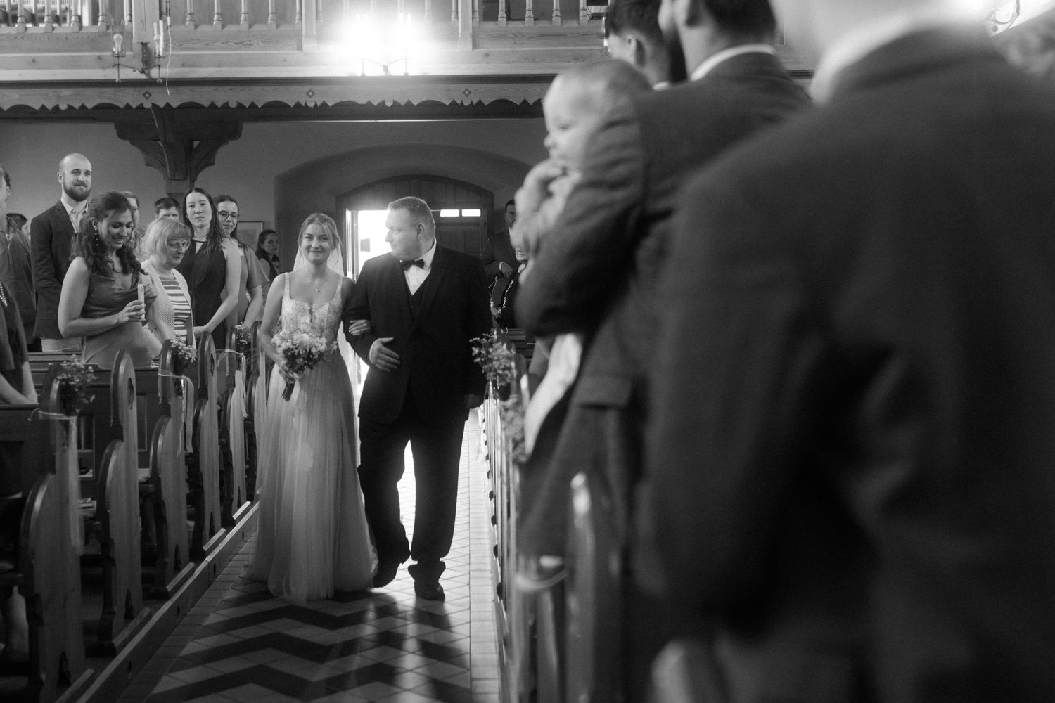 Wedding ceremony procession in a church aisle captured in black and white.
