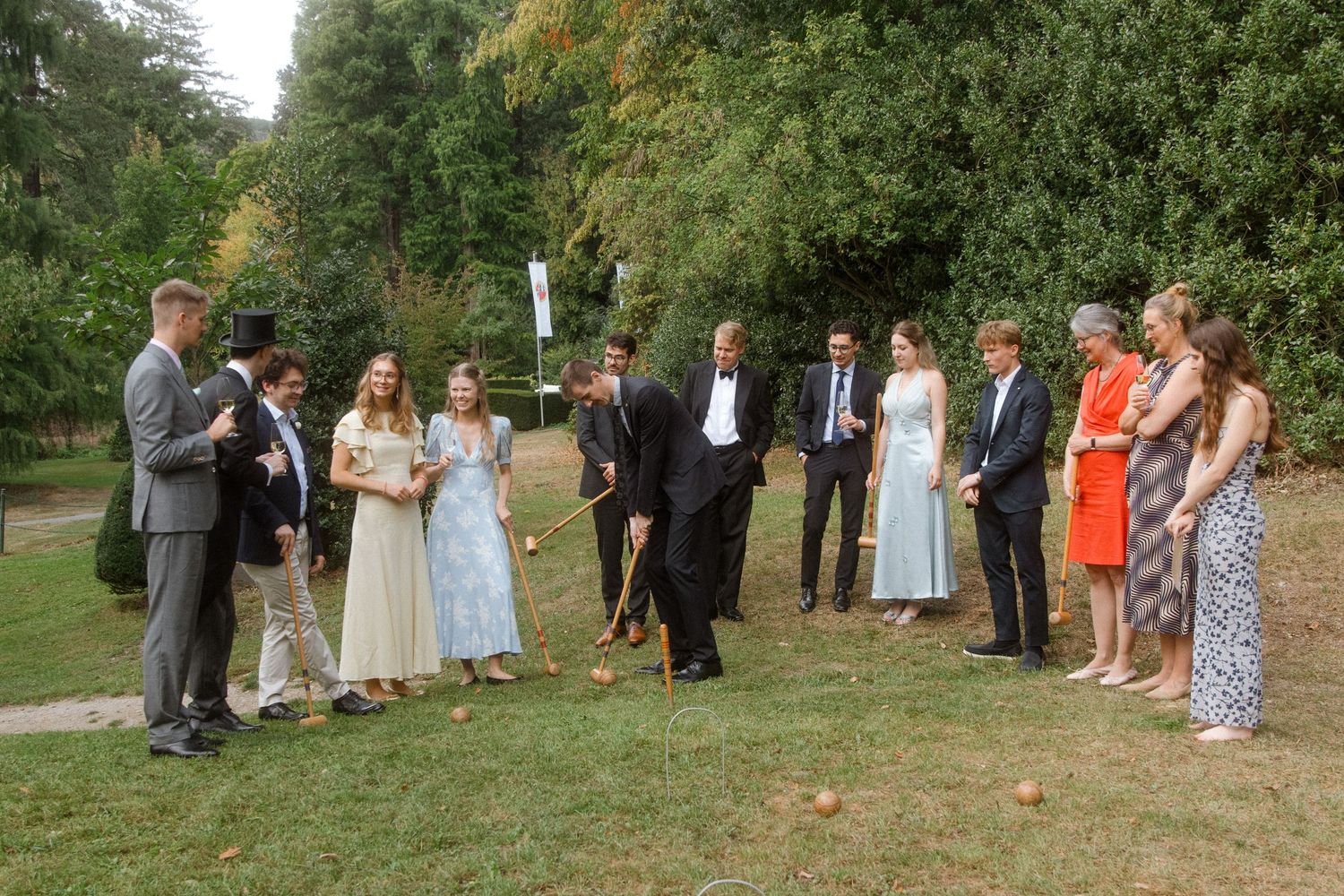 Wedding guests gathered on a lawn watching others play croquet.
