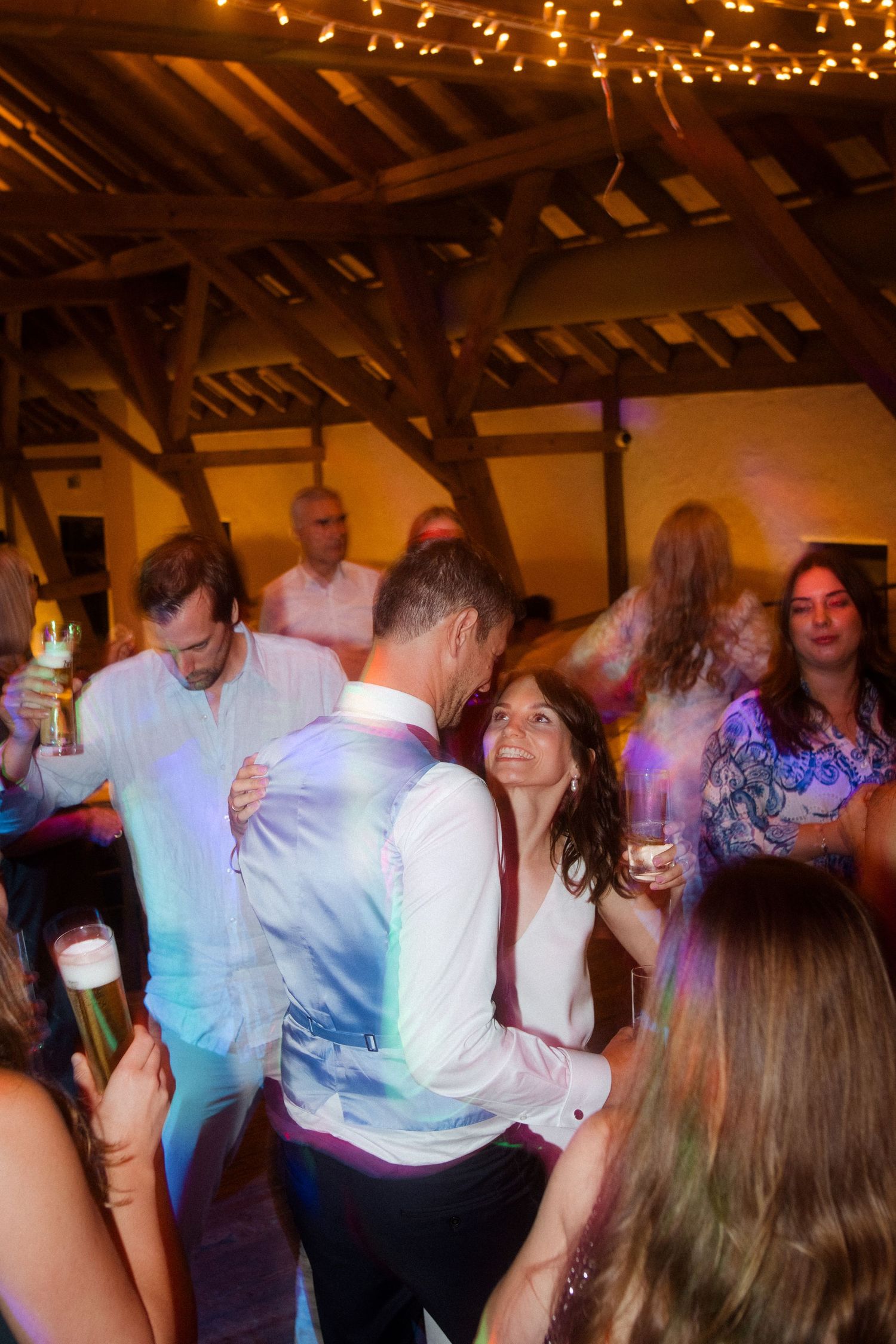 Couples dancing and mingling at a reception under warm string lights.