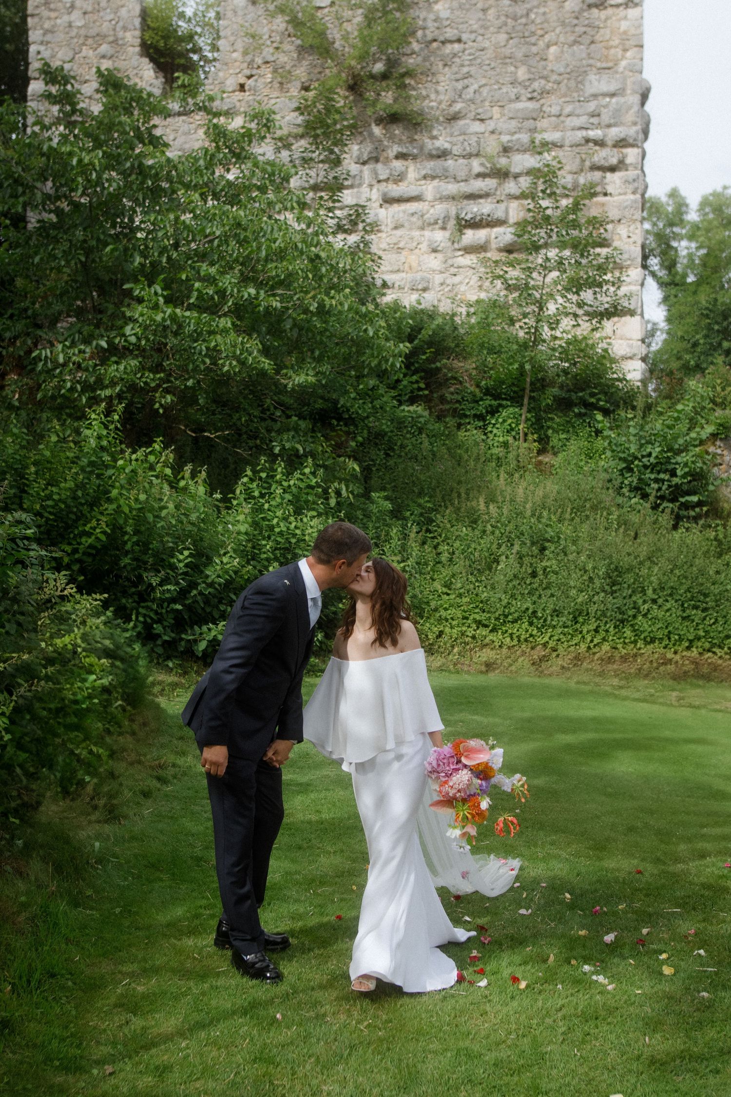 Romantic moment between newlyweds in front of a stone wall during their garden wedding.