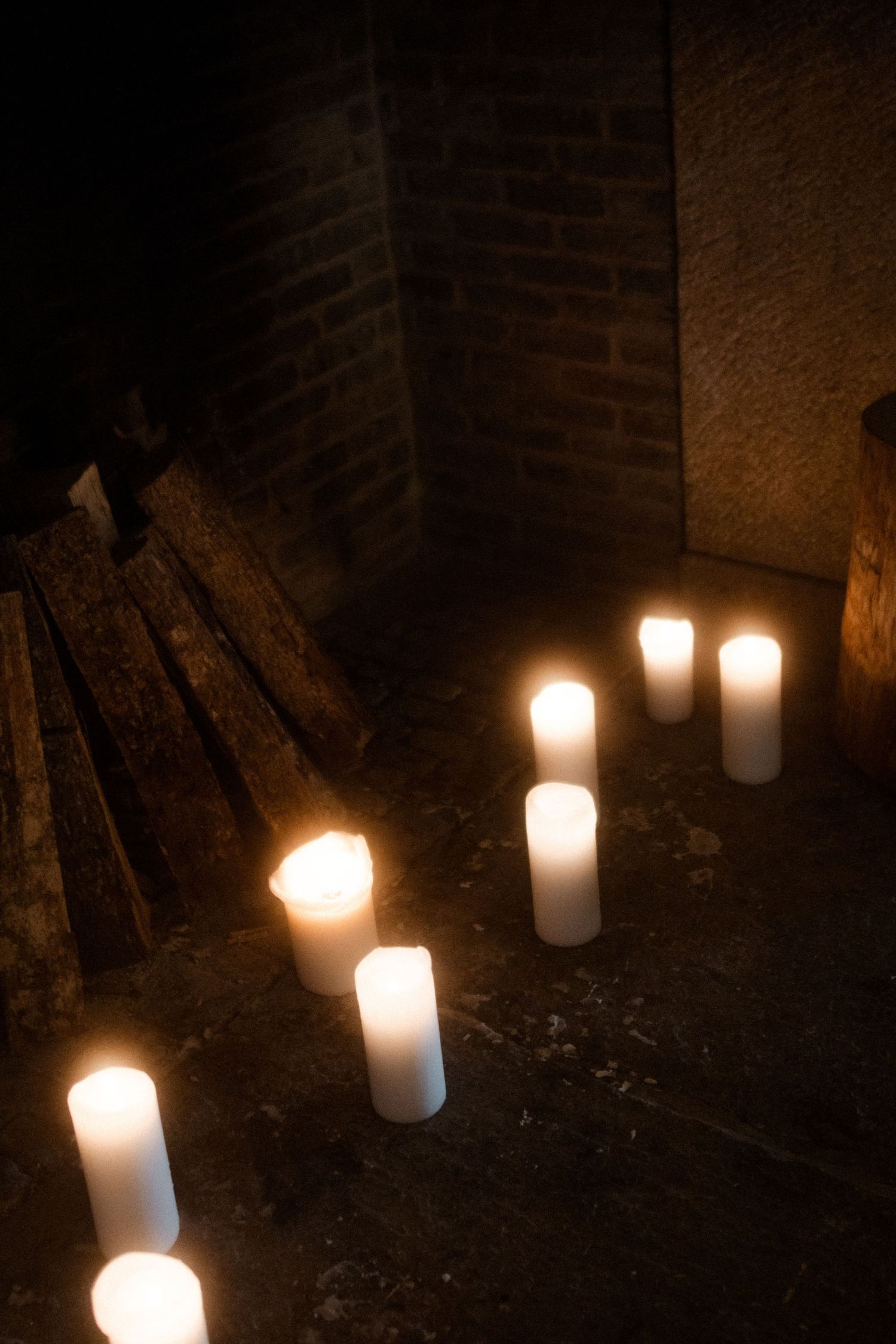 White pillar candles creating romantic pathway lighting in dark brick corner.