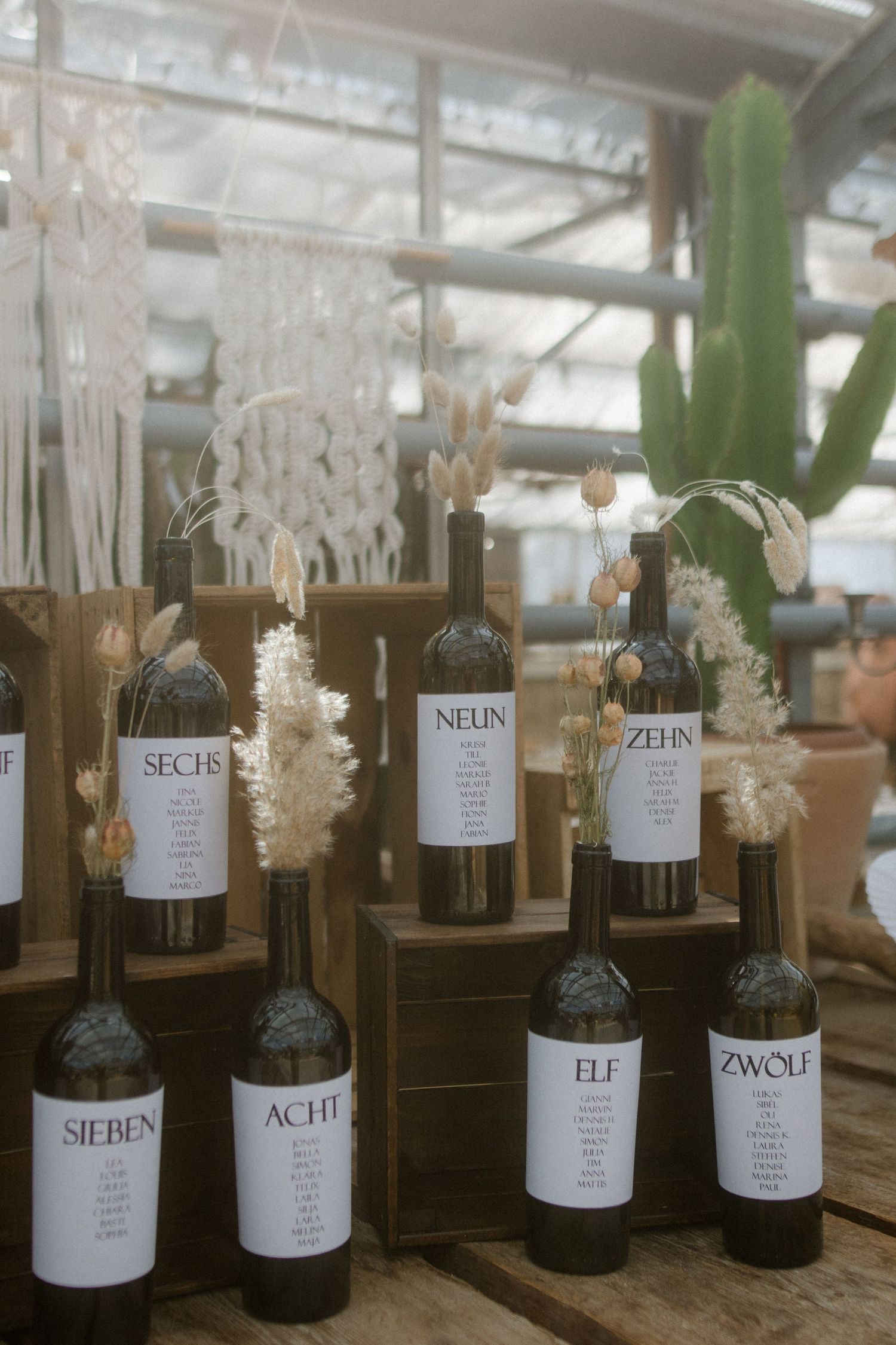 Wine bottles decorated with dried flowers and custom numbered labels displayed on wooden shelving.