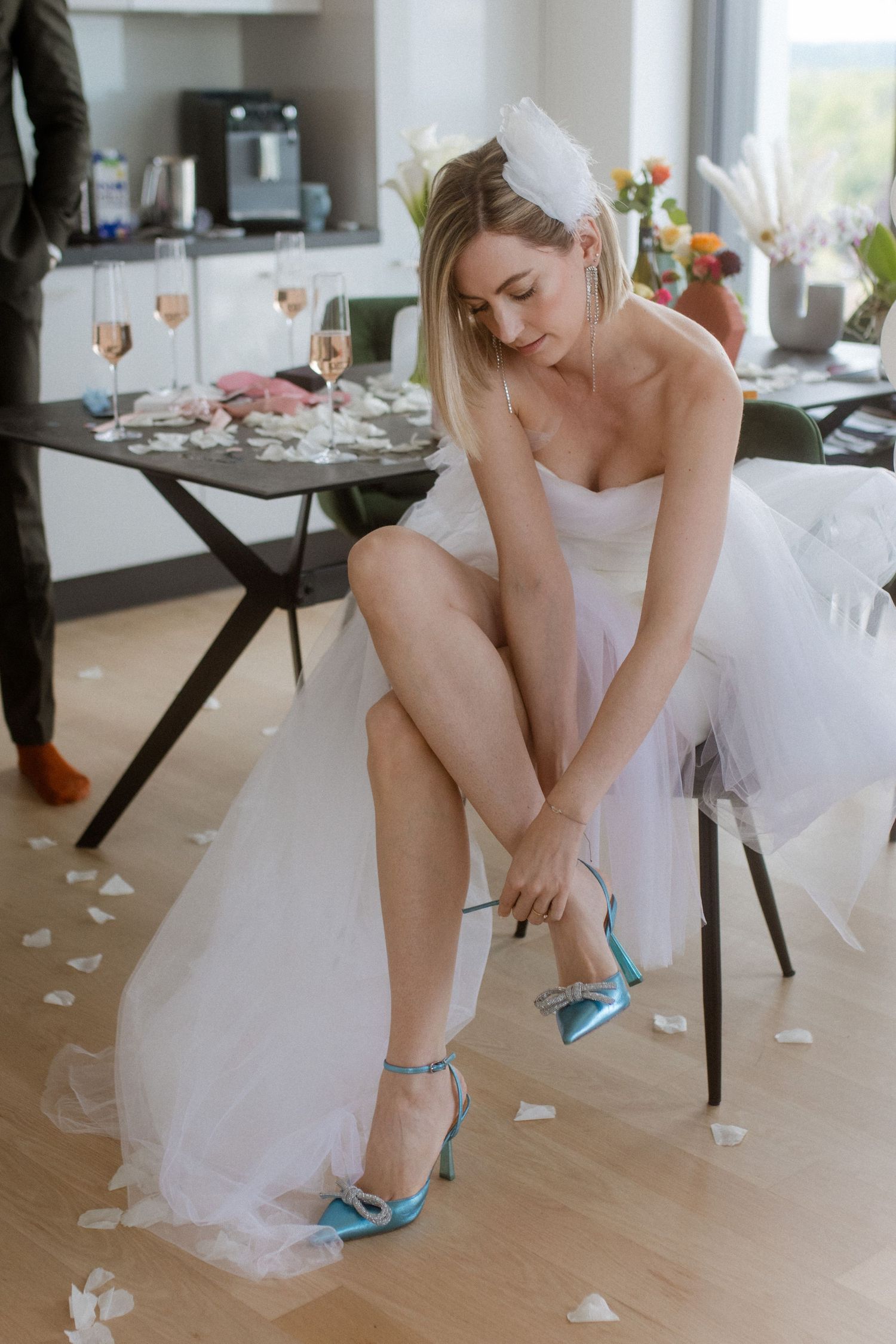 Bride in white dress adjusting turquoise heels with reception table in background.