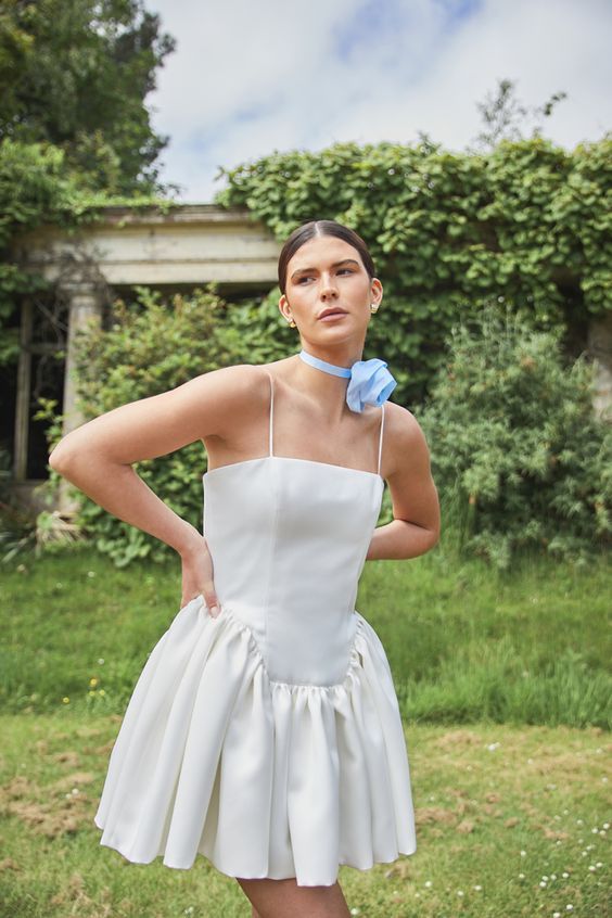 Short white wedding dress with gathered skirt photographed in garden setting.