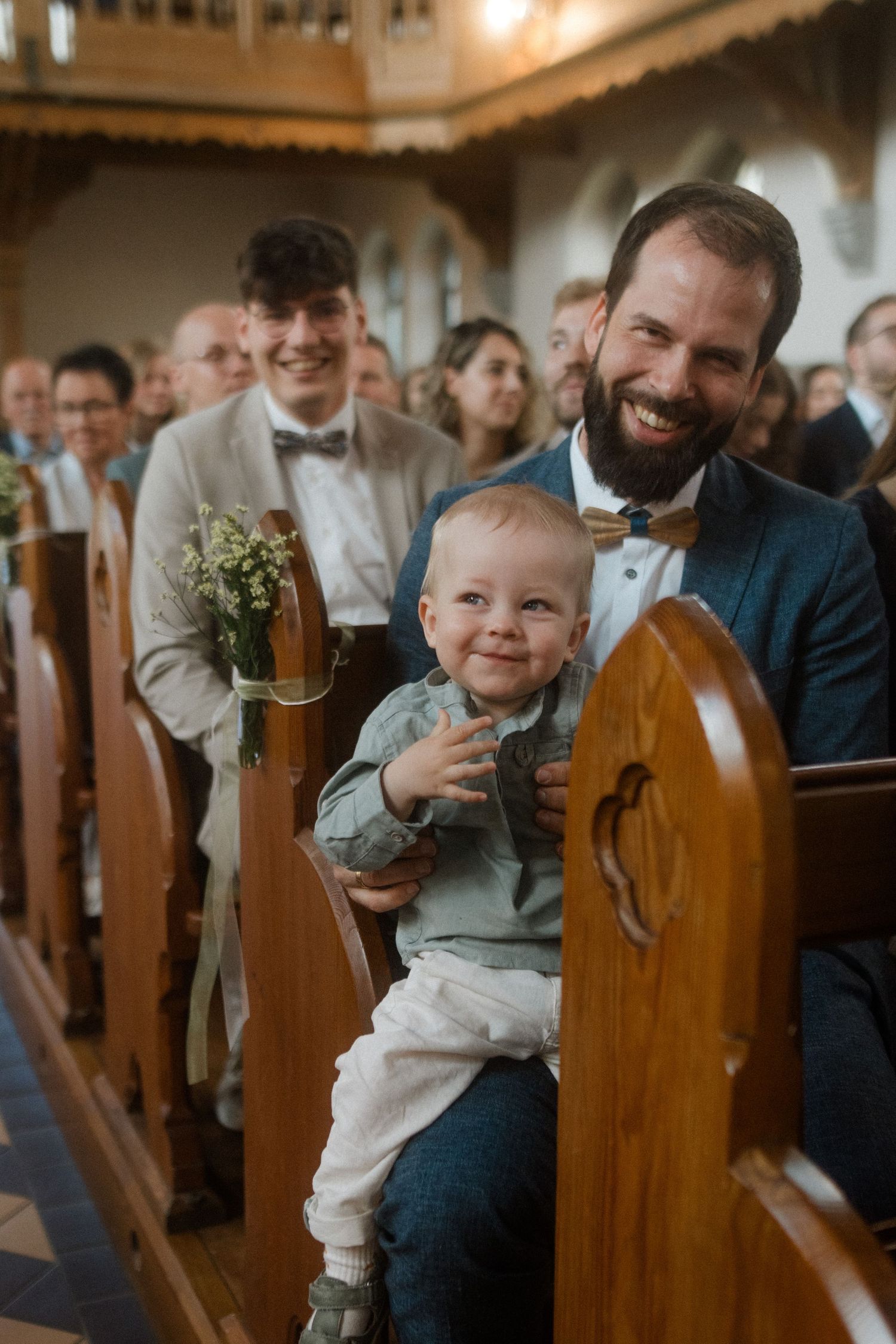 Attendees sit in wooden church pews decorated with simple floral arrangements.