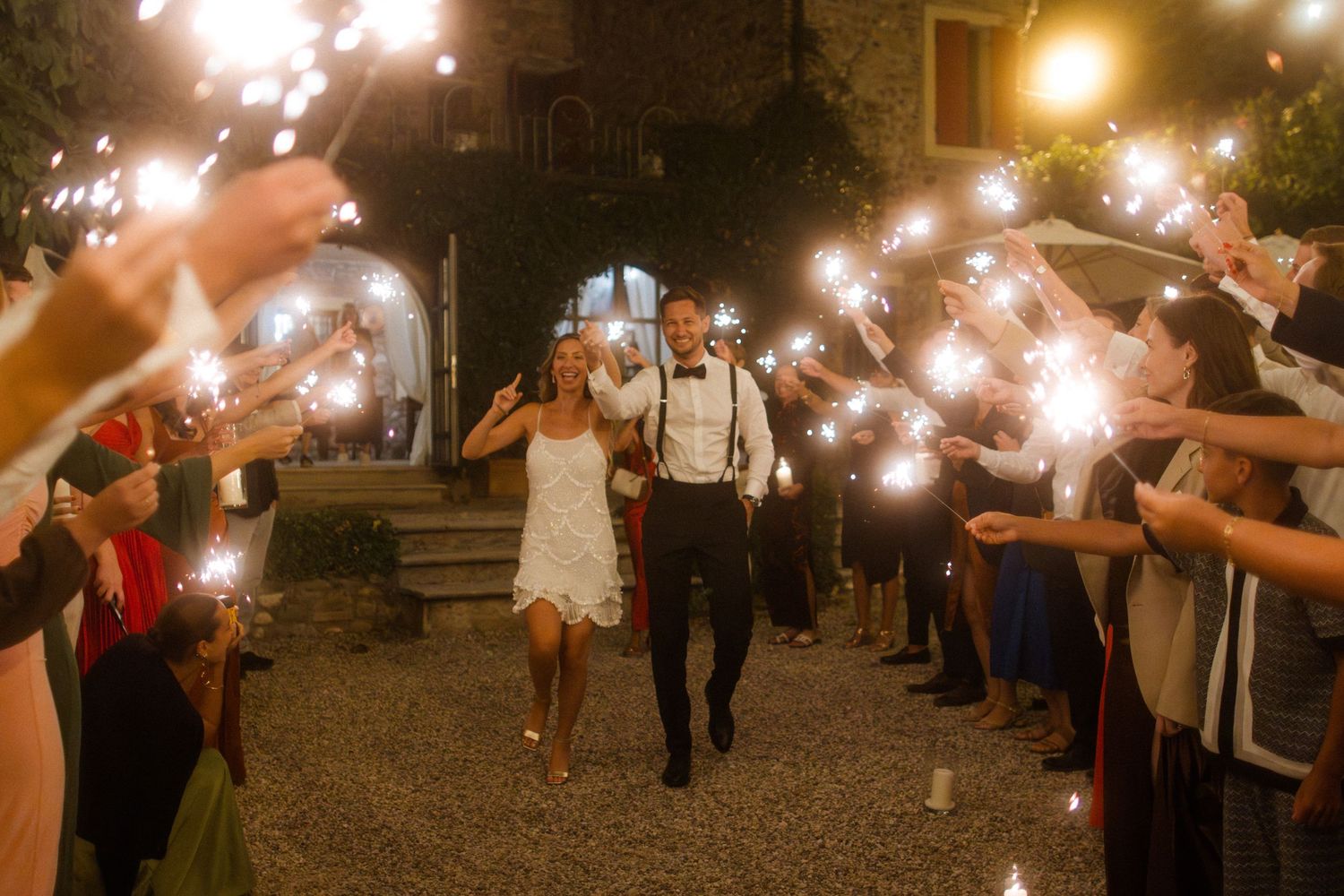 Sparklers illuminate the night as guests form a glowing pathway at a celebration.
