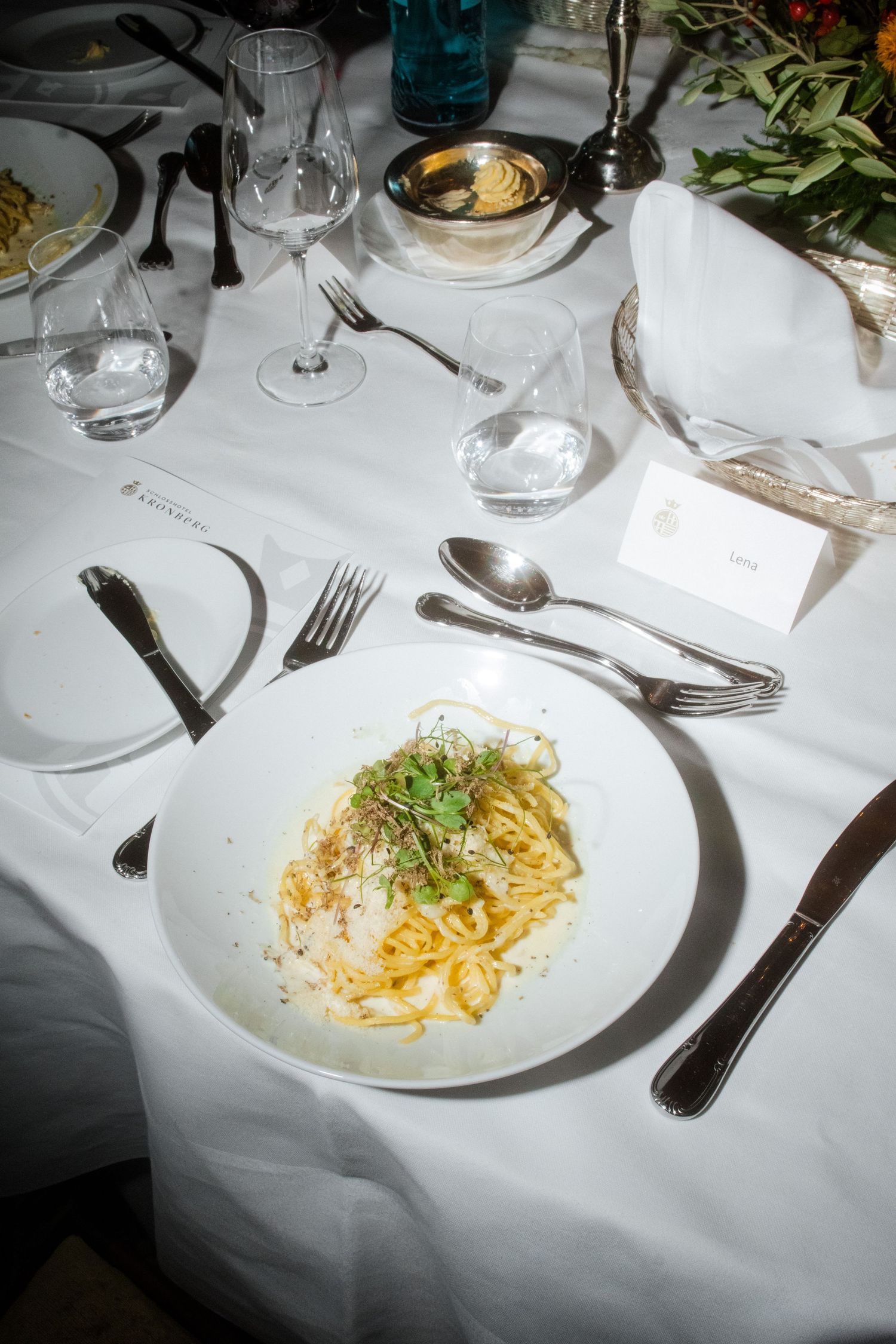 Pasta dish elegantly plated on white tablecloth with formal silverware setting.