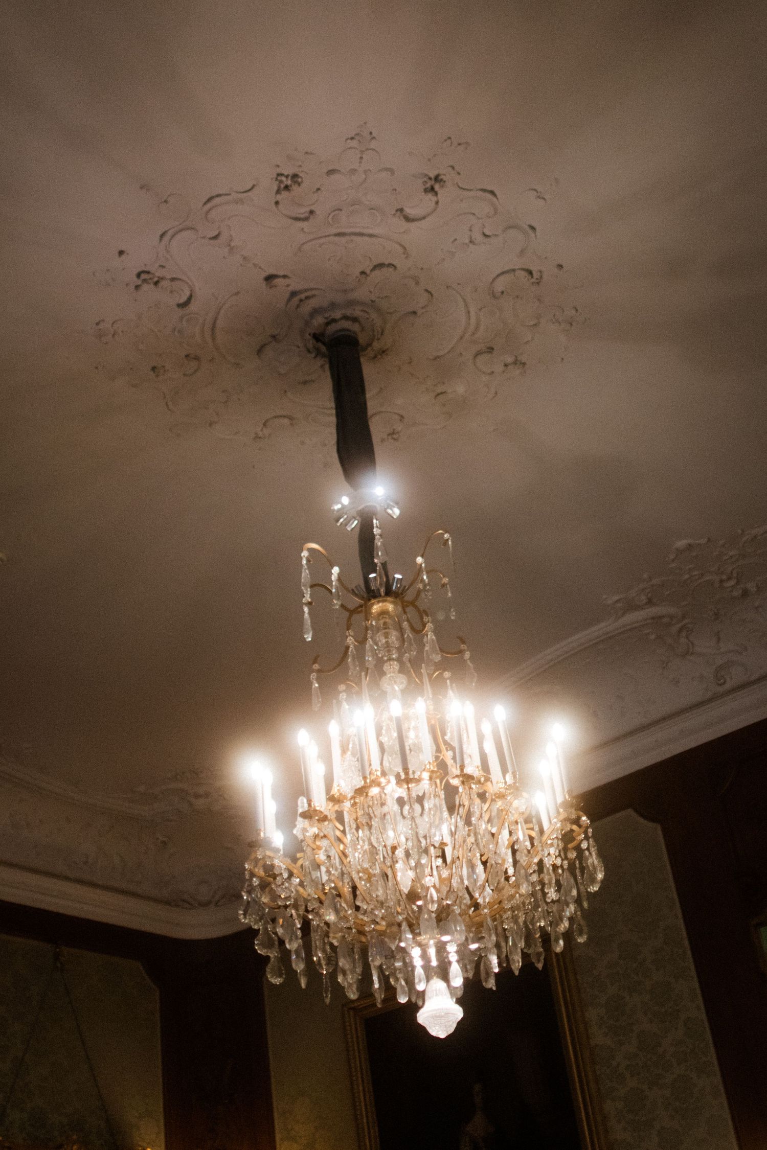 Crystal chandelier illuminated against ornate ceiling with decorative molding.