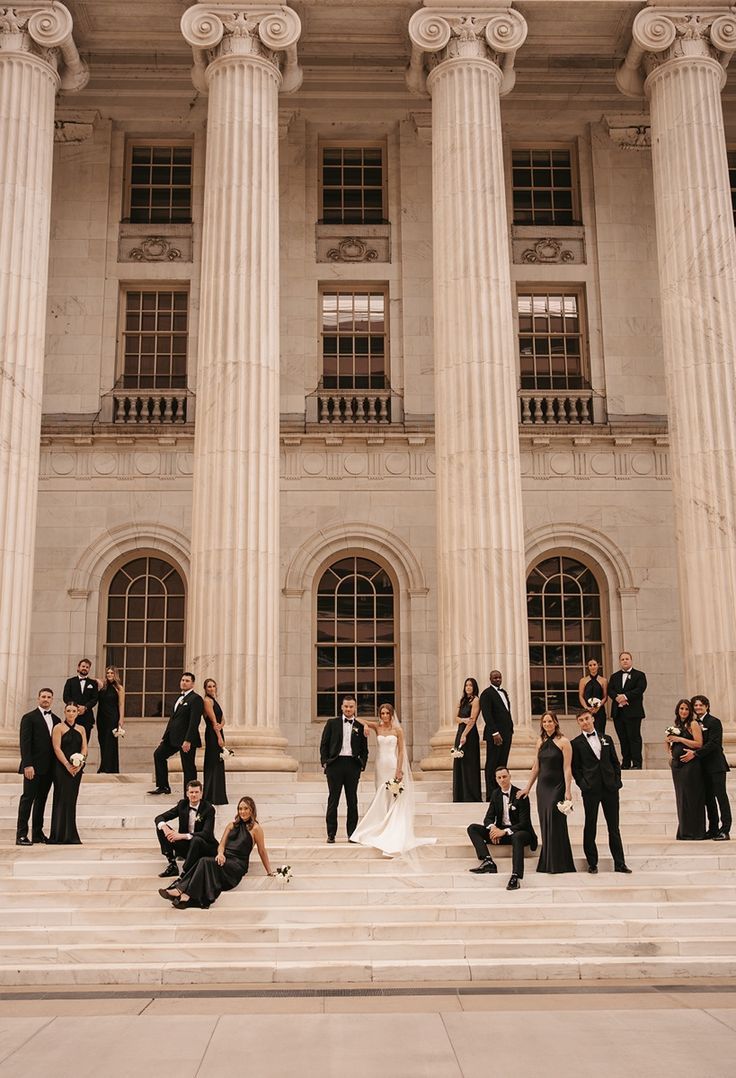 Wedding party arranged on grand stone steps of classical building with ionic columns.