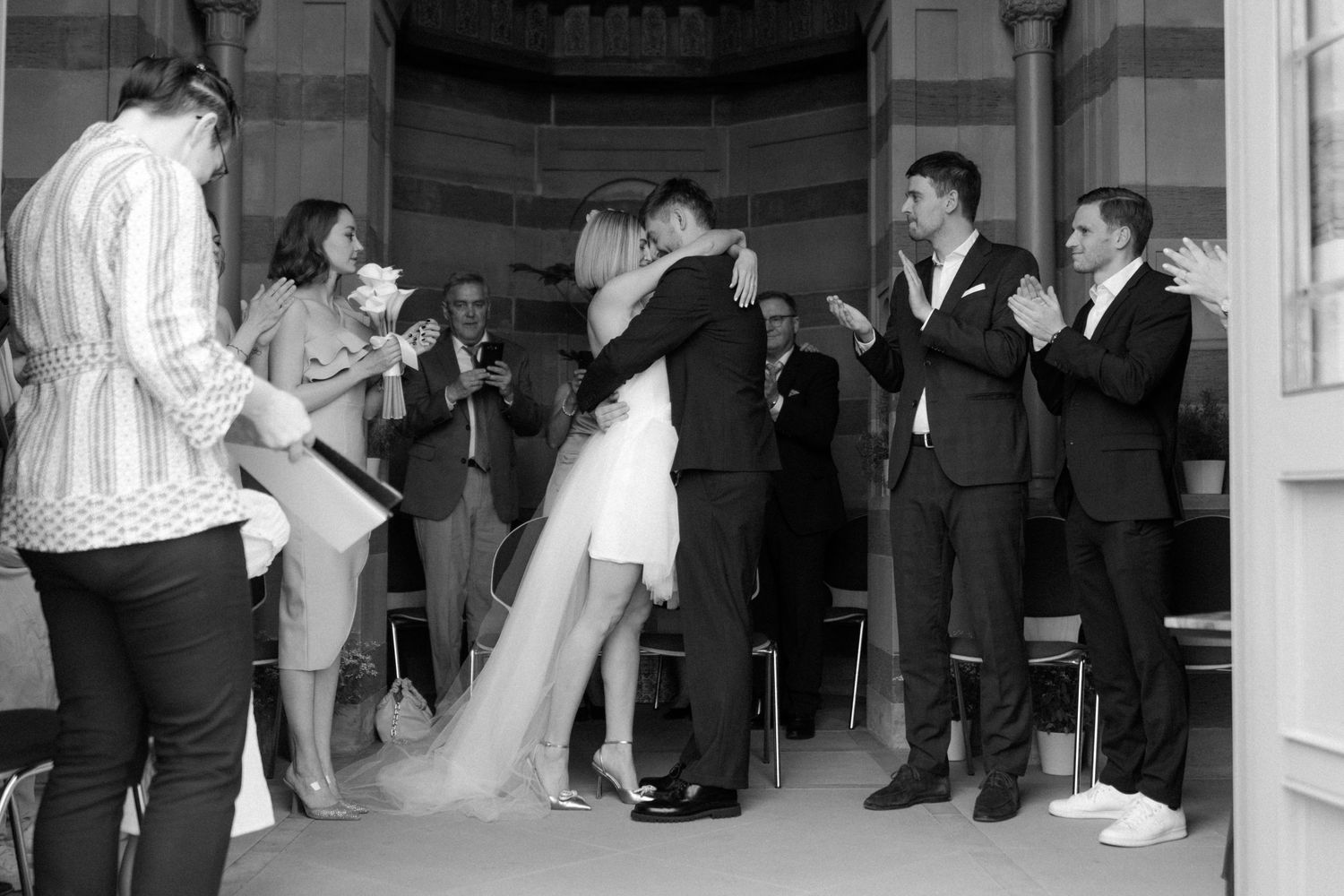 Wedding party celebrates and applauds newly married couple during intimate ceremony.