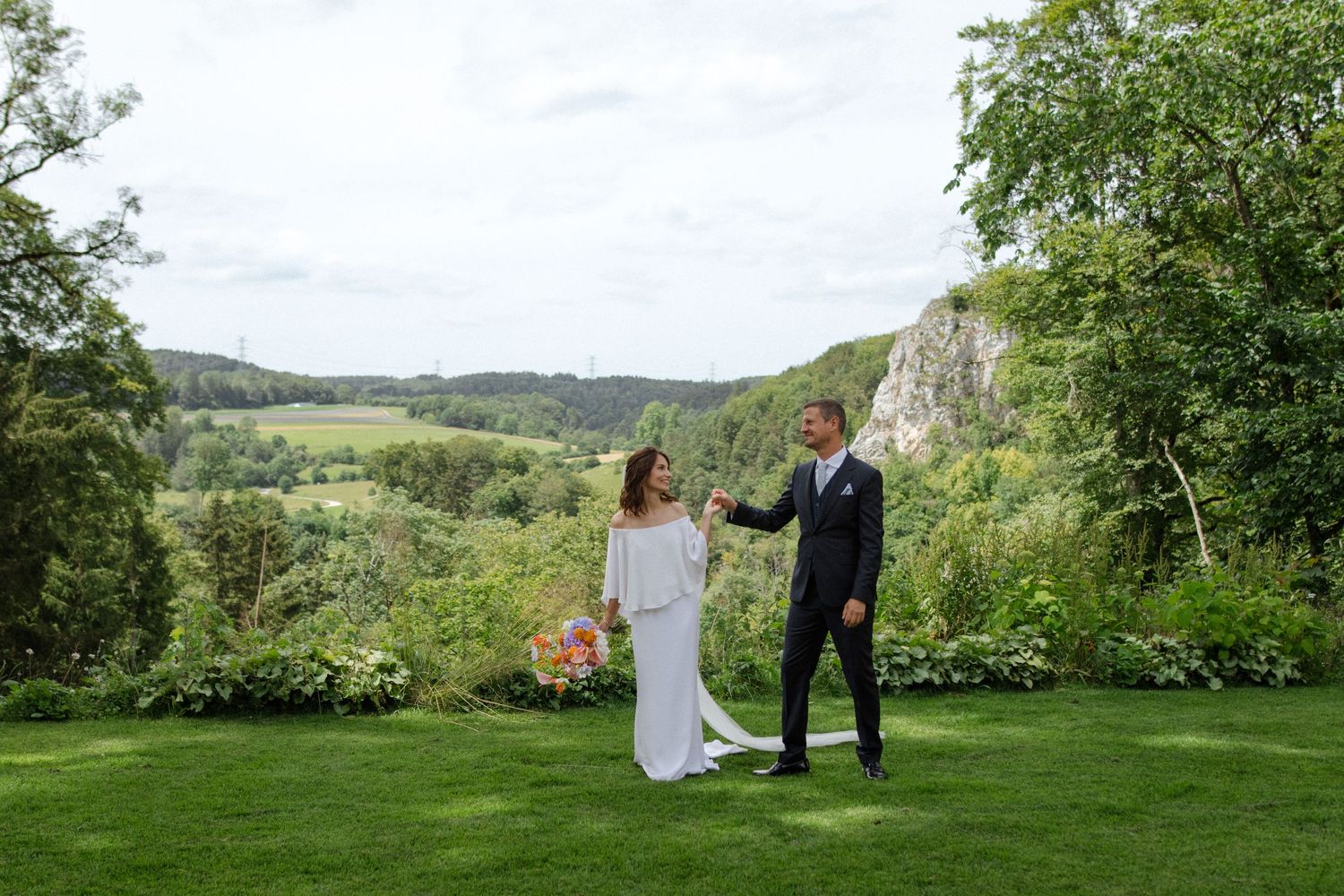 Newlyweds dance together on a manicured lawn with dramatic cliffs in the background.