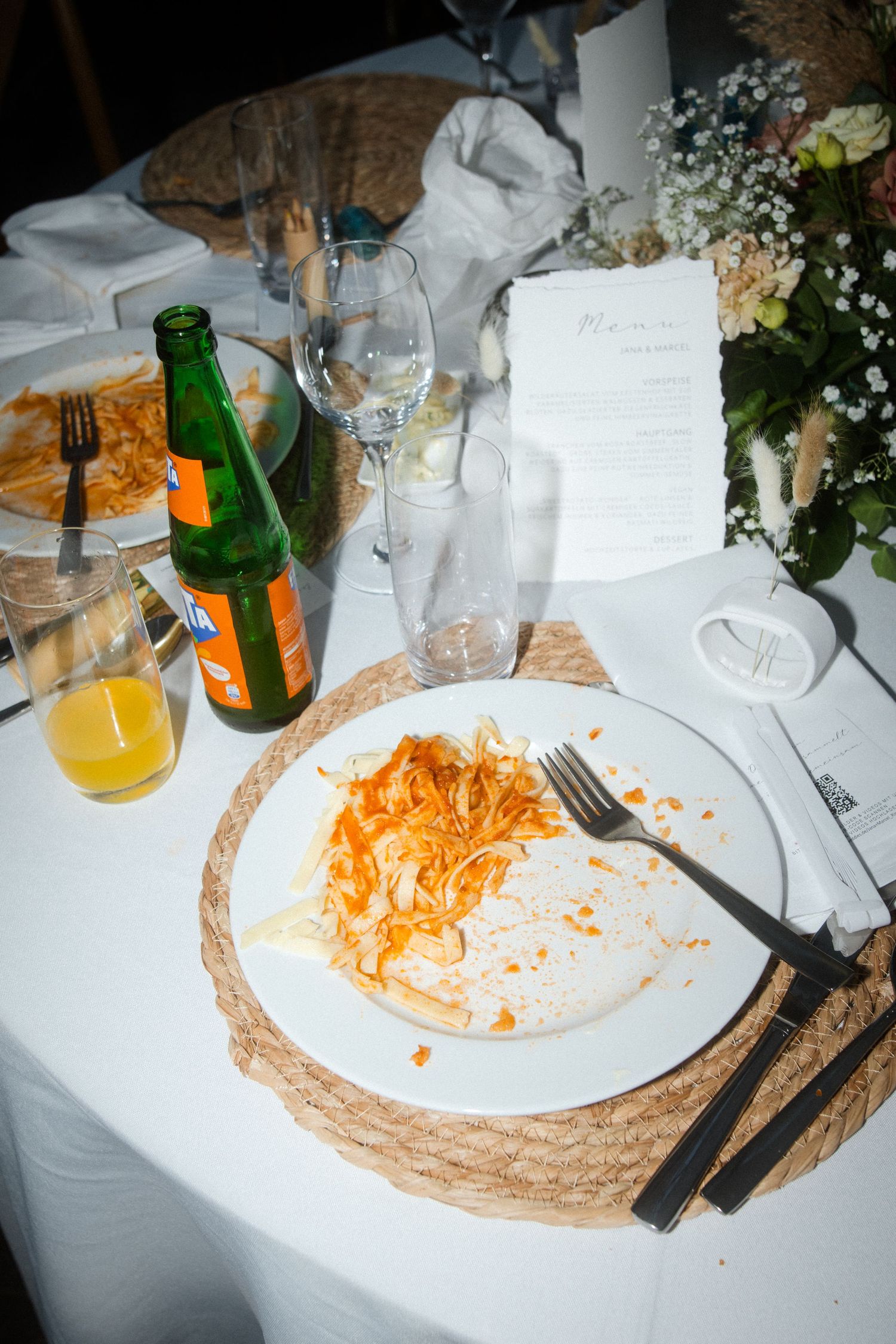 Used dinner plates and beverages on white tablecloths at a wedding reception.