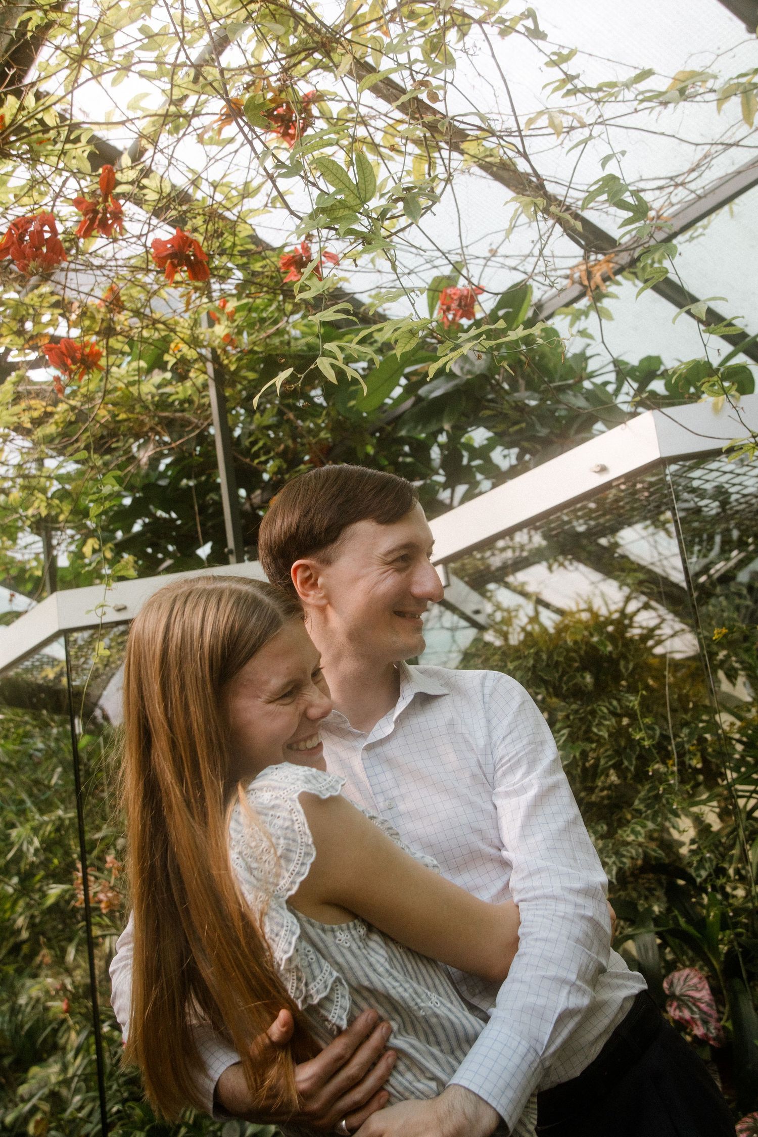 Romantic greenhouse photoshoot with greenery and red flowers in background.