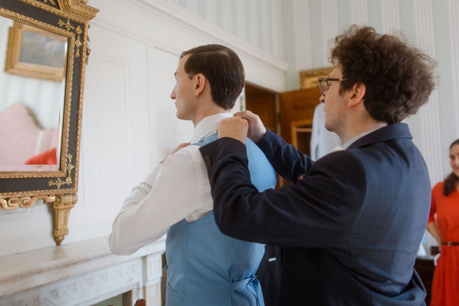 Two people in formal attire interacting in a bright white room with gold-framed artwork.