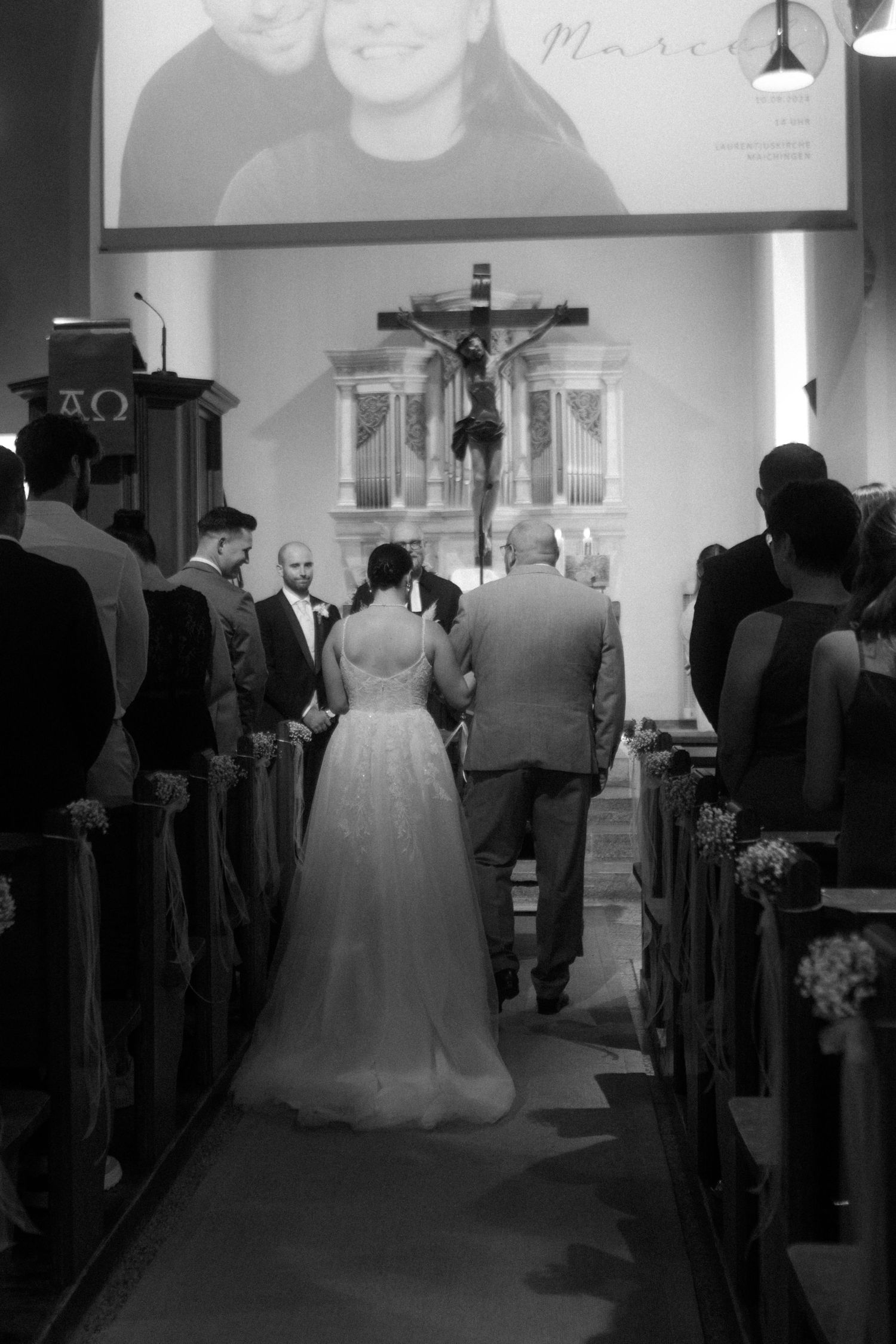 Church wedding ceremony with crucifix altar and wooden pews in black and white.