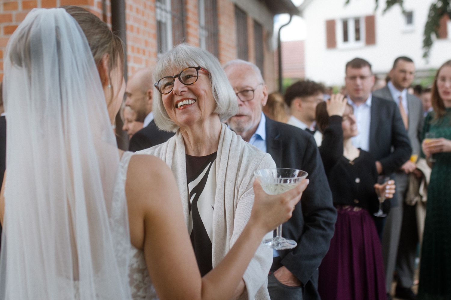 Wedding guests sharing joyful moment during outdoor reception by brick building.