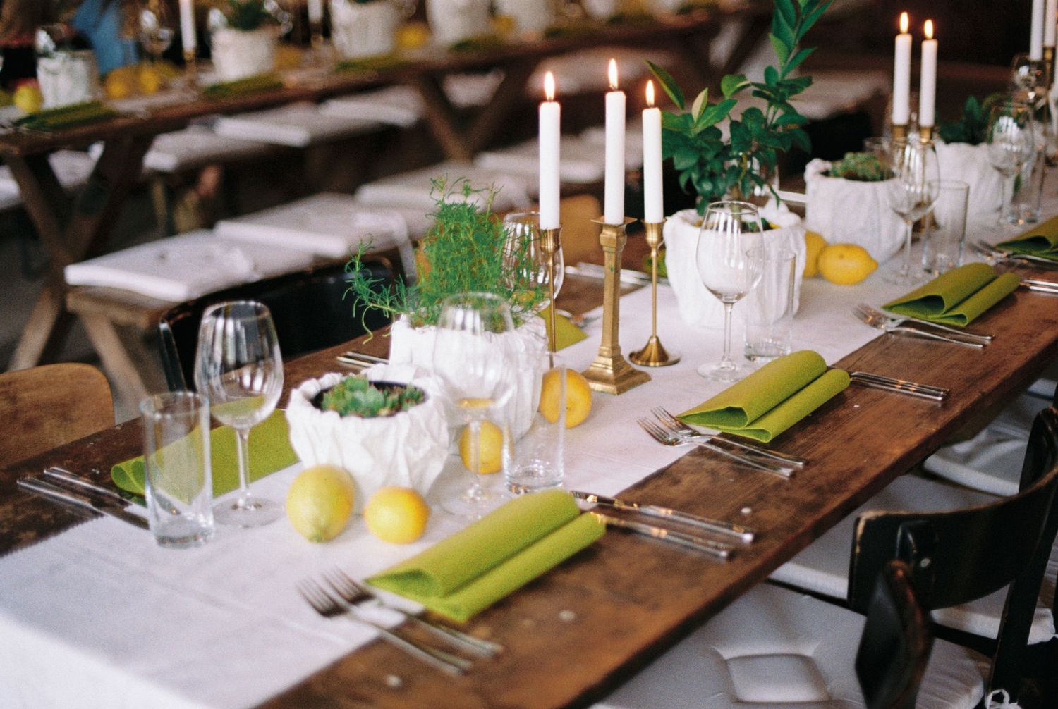 Wedding reception table decorated with candles, citrus accents, and green linens on wooden surface.