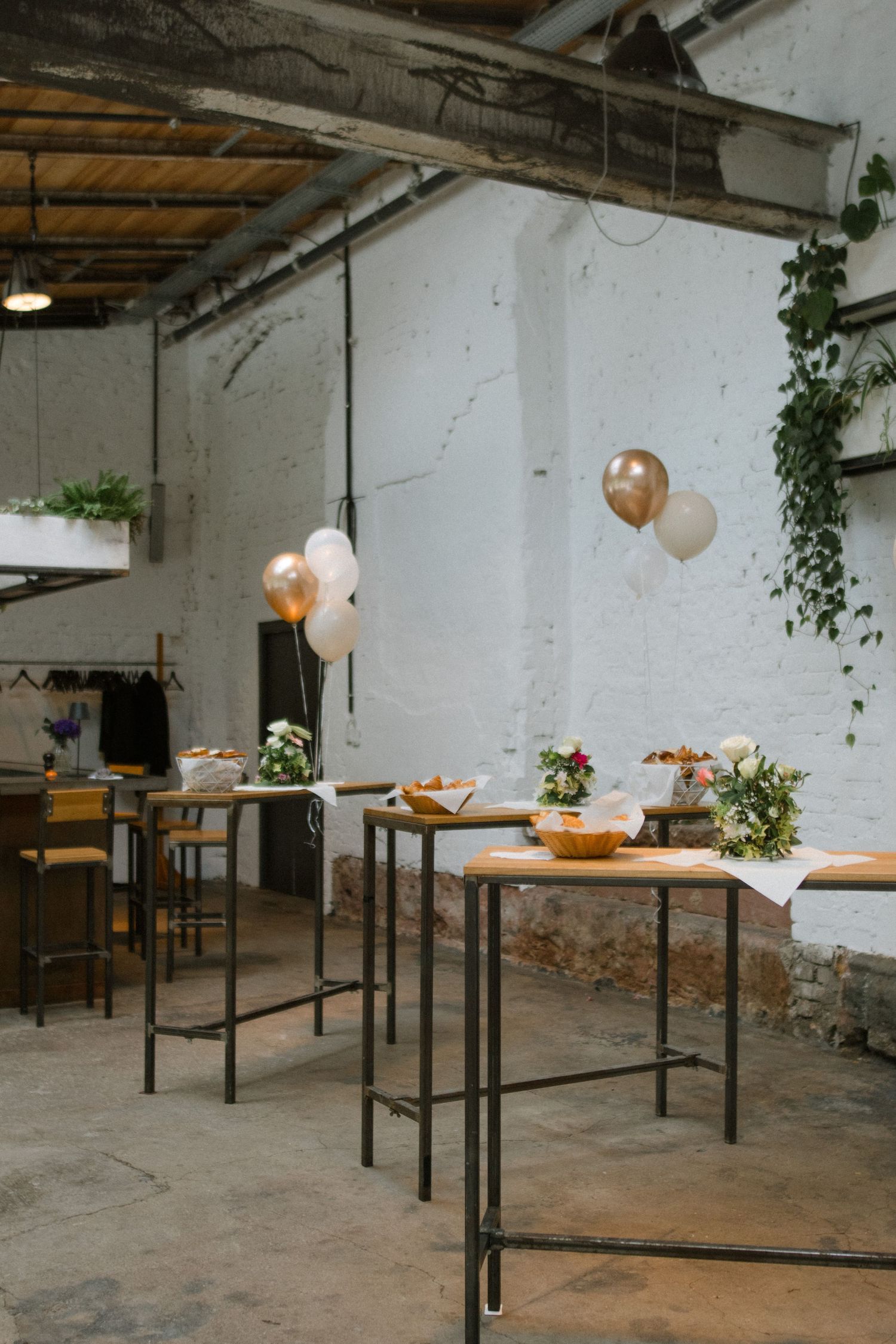 An industrial event space decorated with high tables, balloons and greenery.