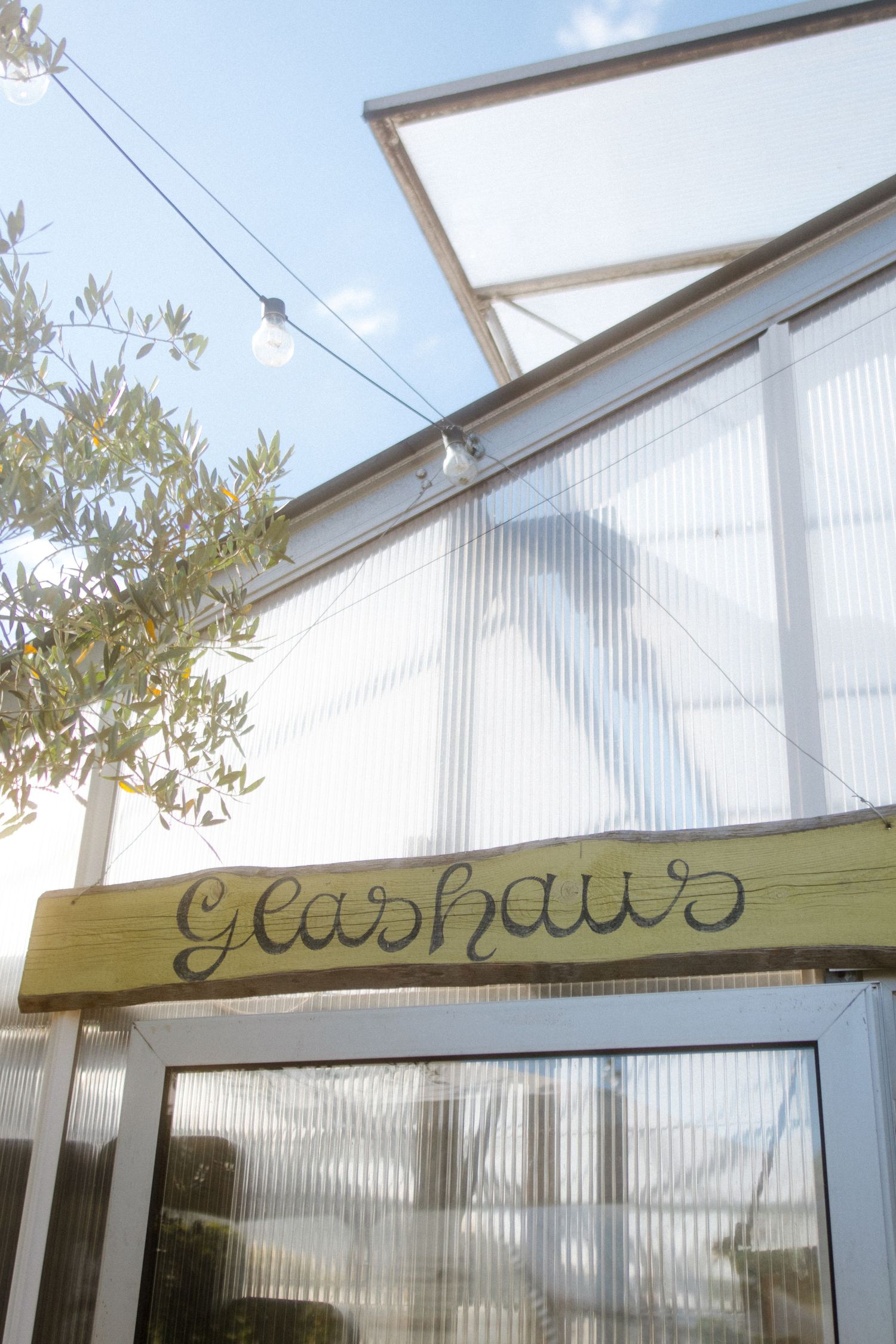 A wooden sign with 'Glashaus' text mounted above a greenhouse-style entrance.