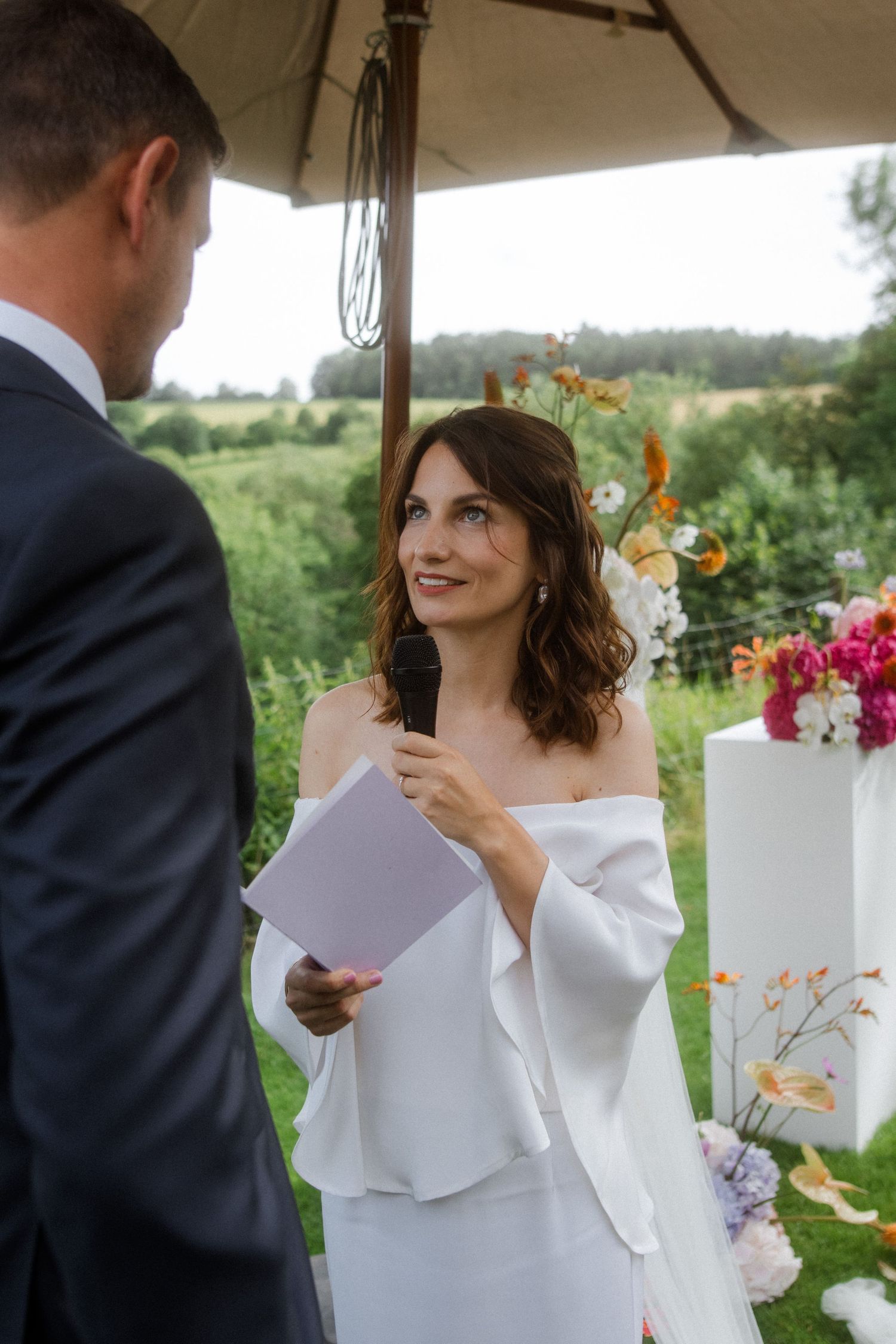 Couple exchanging vows during an outdoor ceremony with floral decorations and countryside views.