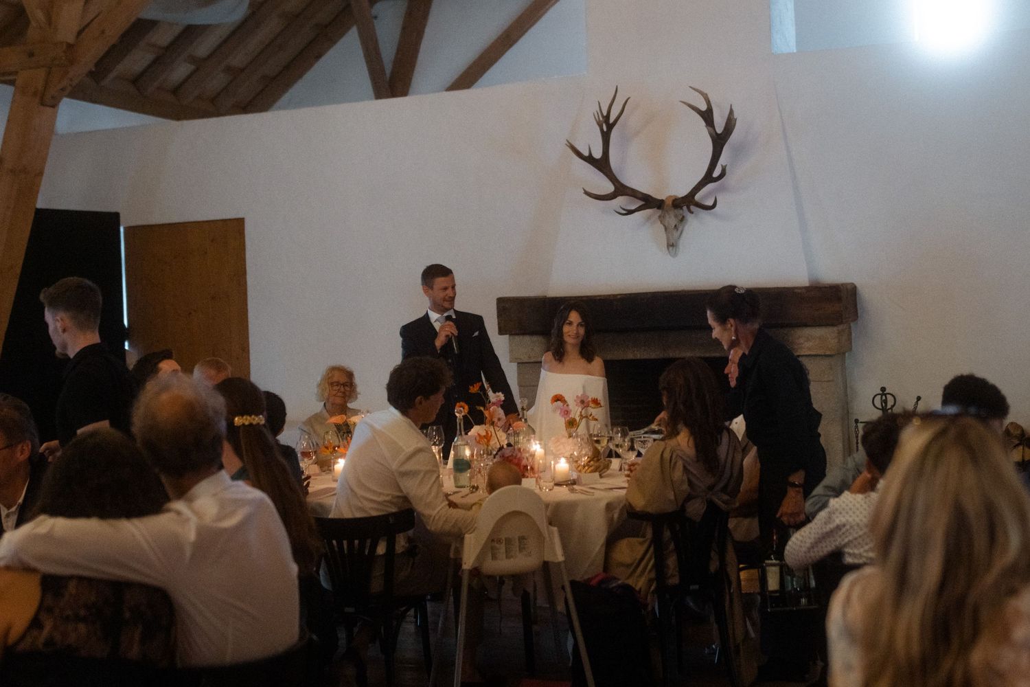 Wedding dinner scene in rustic venue with exposed beams and deer antler wall decor.
