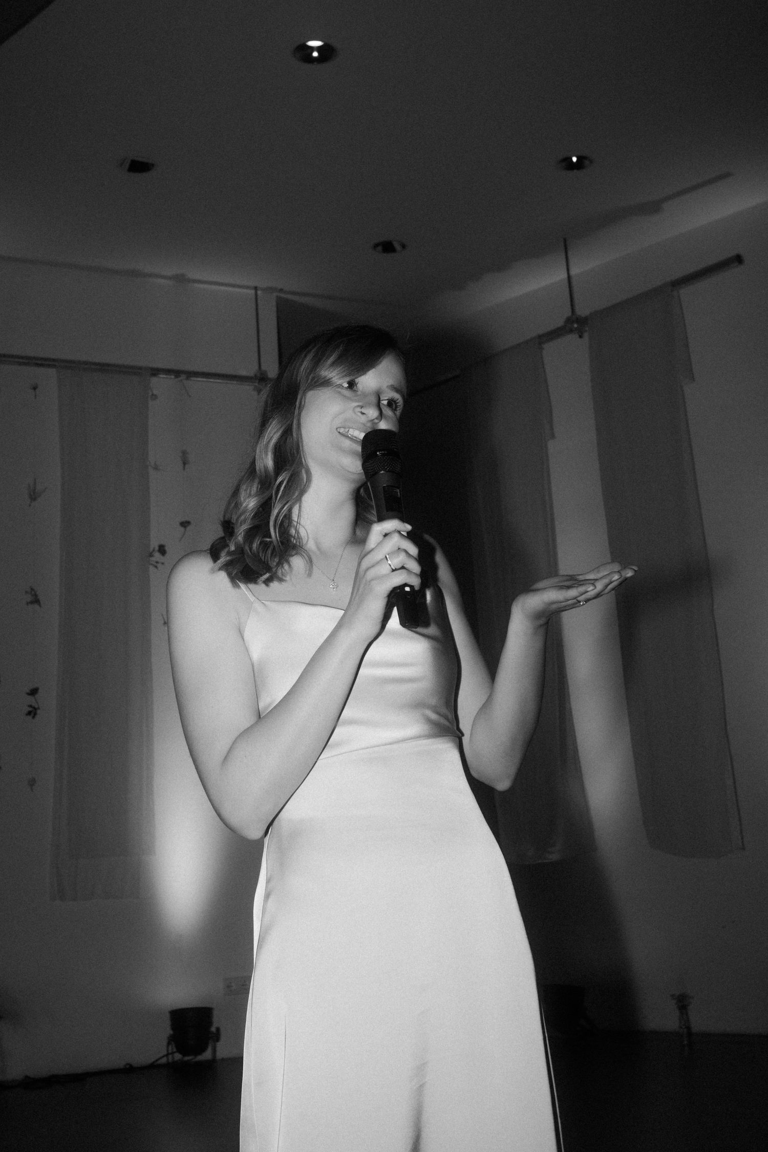 A performer in a white dress sings into a microphone on stage.