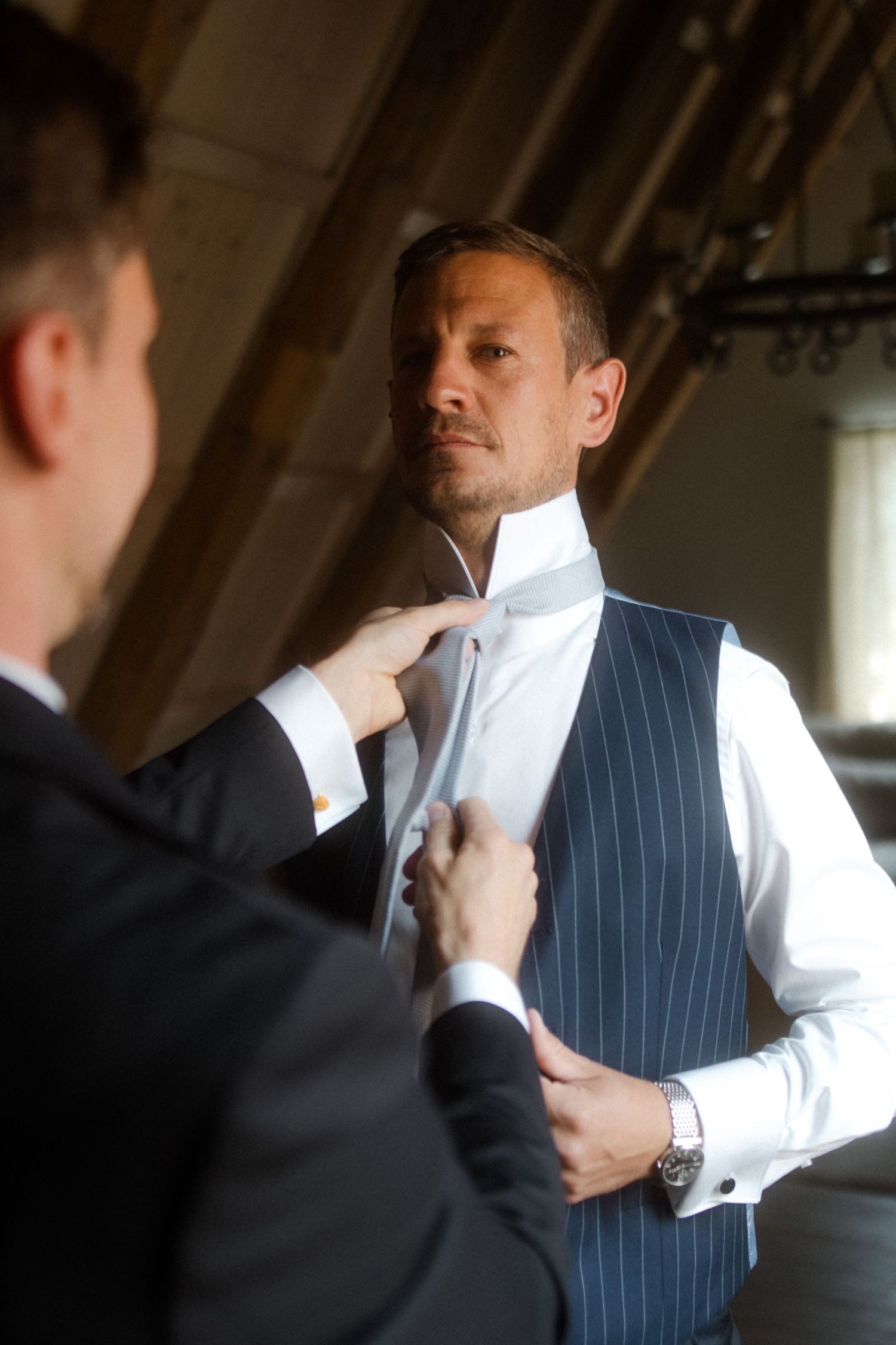 Person being fitted for a pinstripe vest in an attic room.