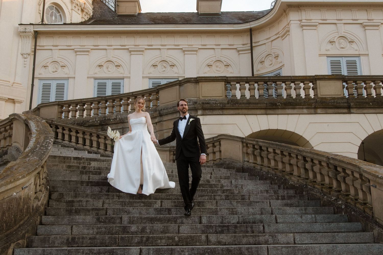 Wedding couple ascending grand stone steps of a classical building.