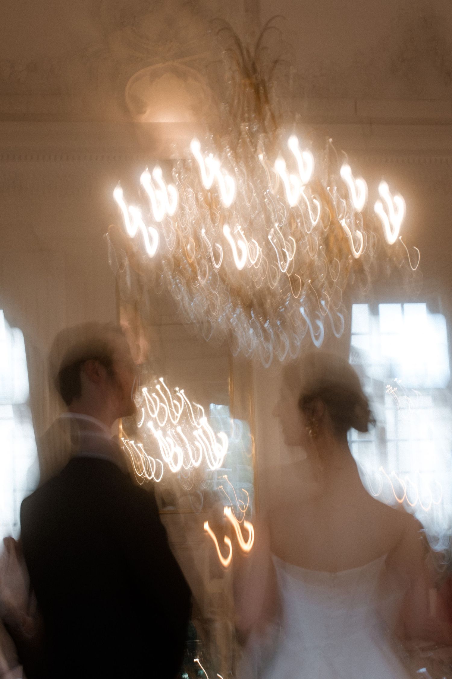 Blurred motion shot of wedding guests dancing under ornate crystal chandeliers.