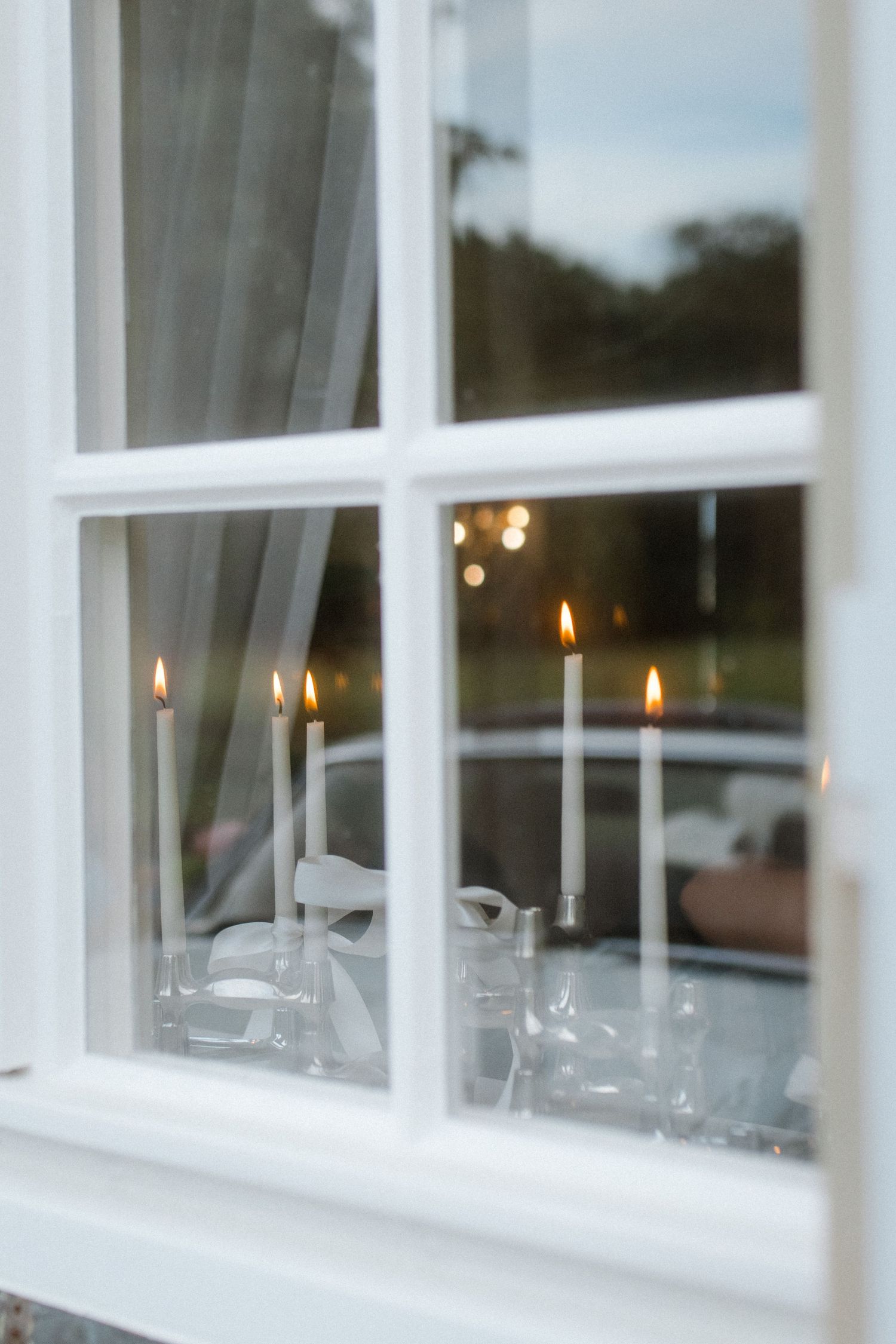 Candlelit window sill with multiple glowing flames reflecting in the glass panes.