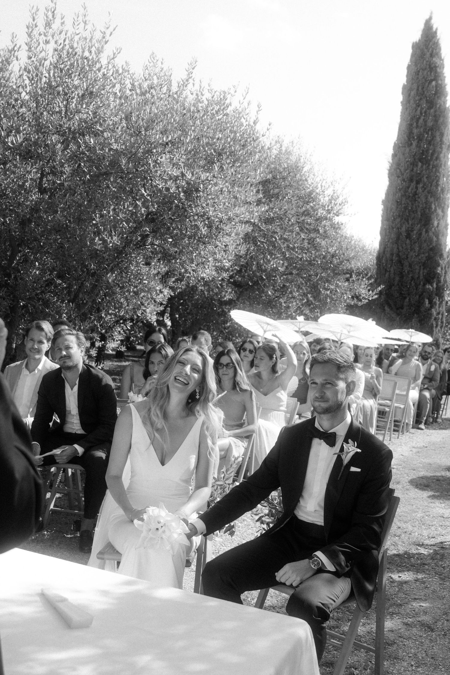 Wedding celebration in a sun-dappled Italian garden with cypress trees.