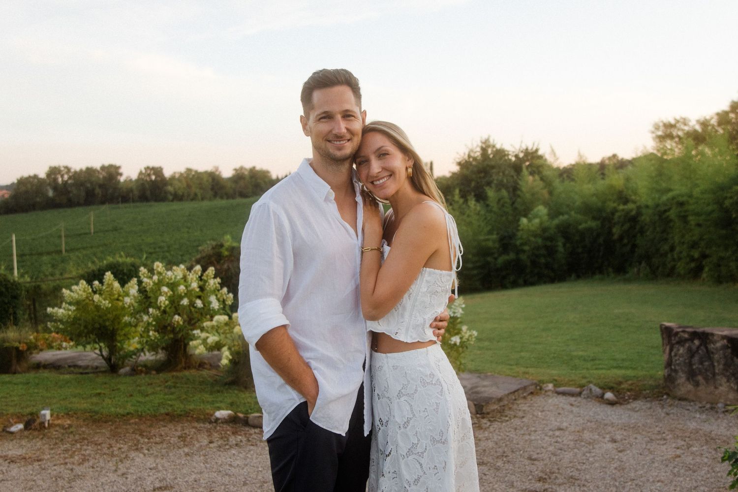 A couple poses together in a scenic outdoor setting during golden hour.